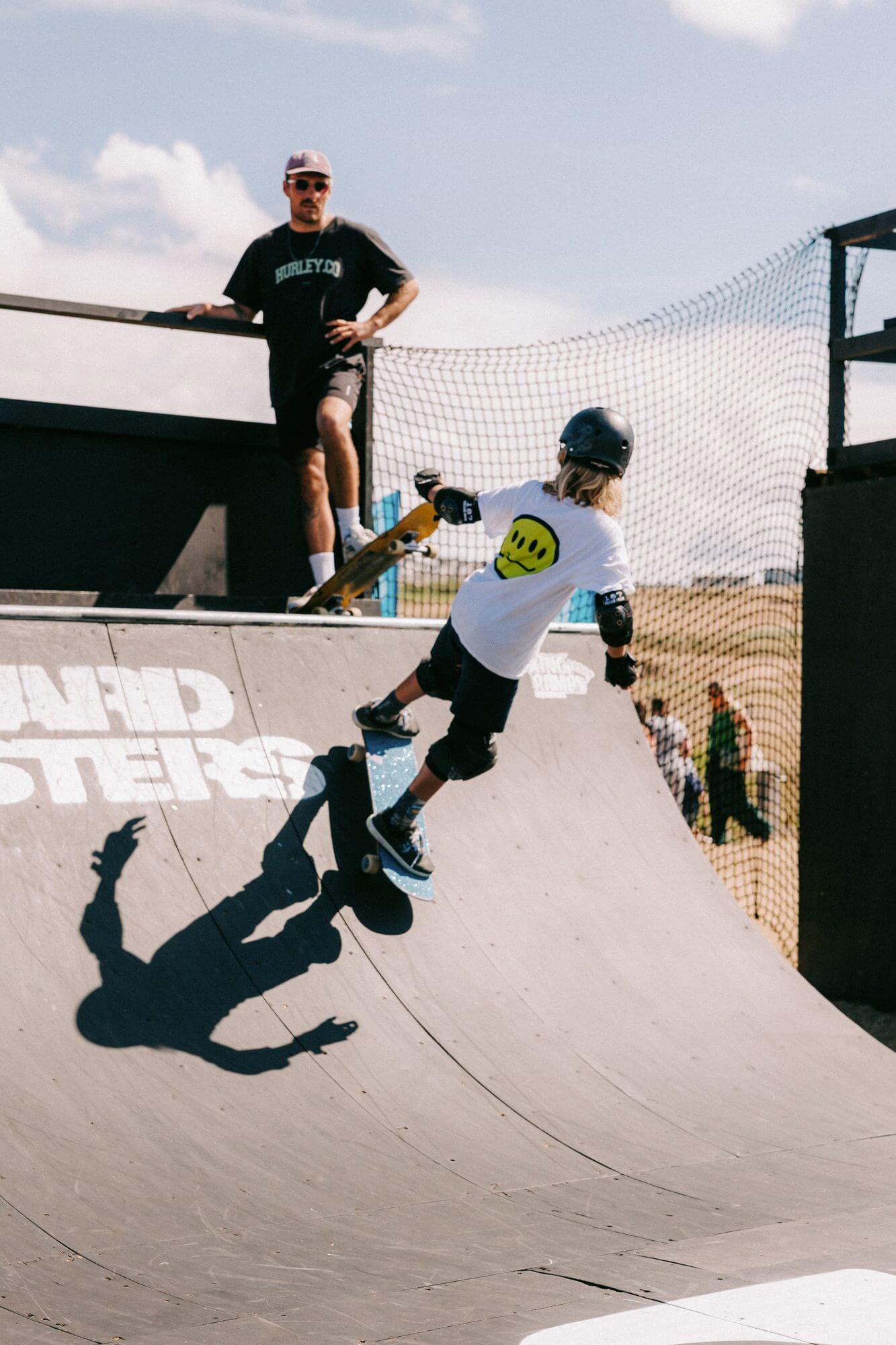 A young skater drops in on the Boardmasters mini ramp watched by a coach