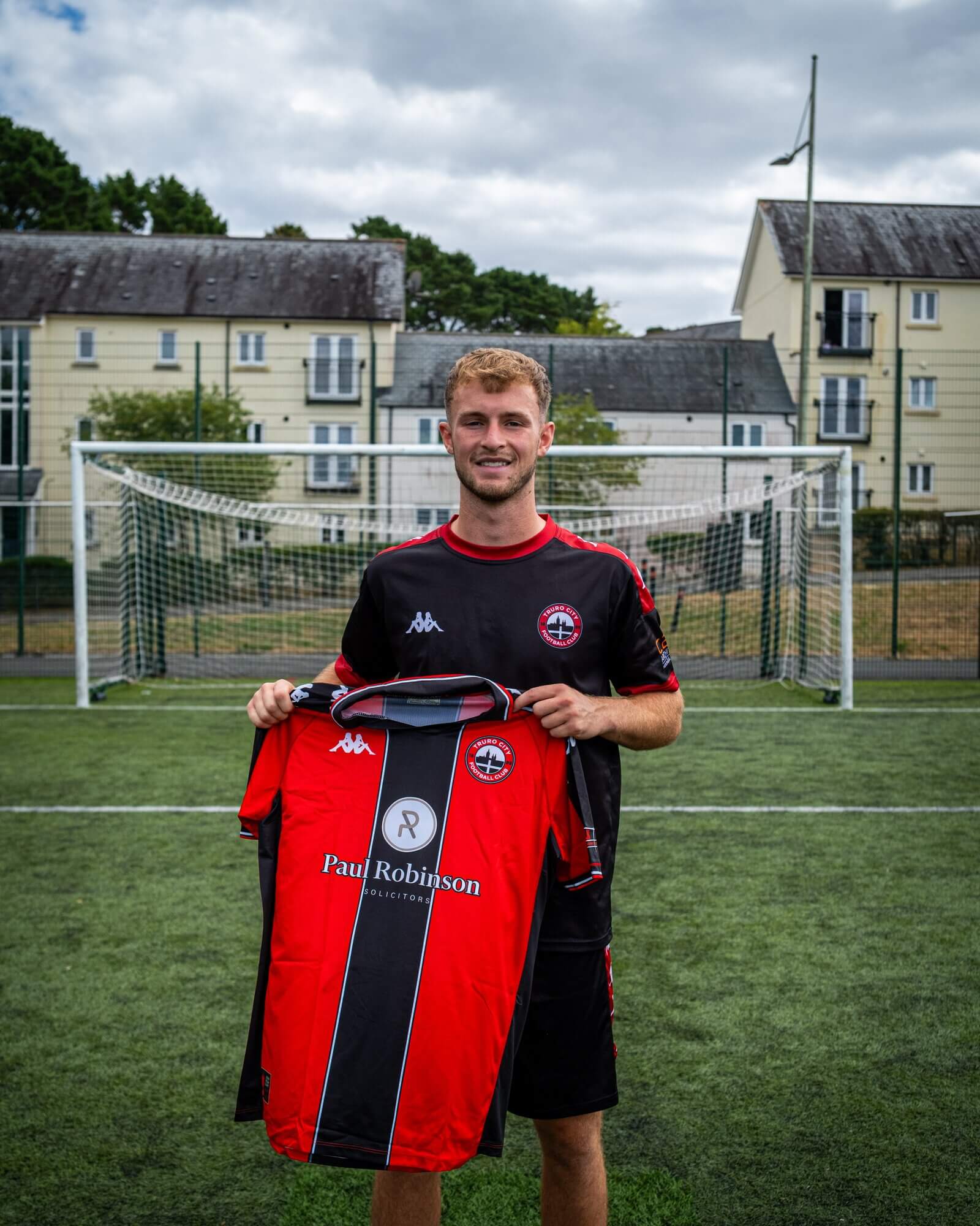 Max Kinsey smiling as he holds up the Truro City home shirt