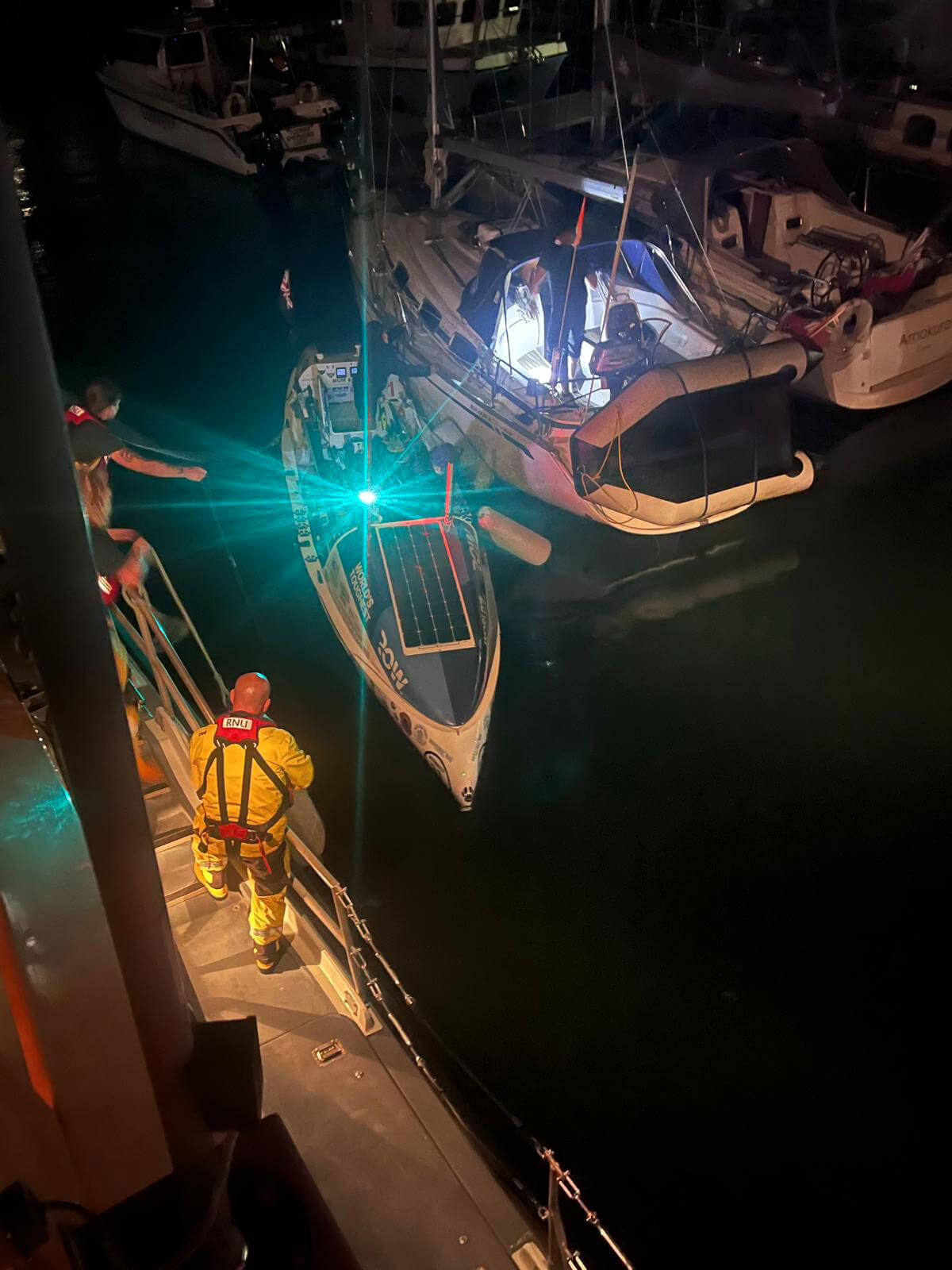 An RNLI crew member climbs down towards the rowing boat alongside the lifeboat at night