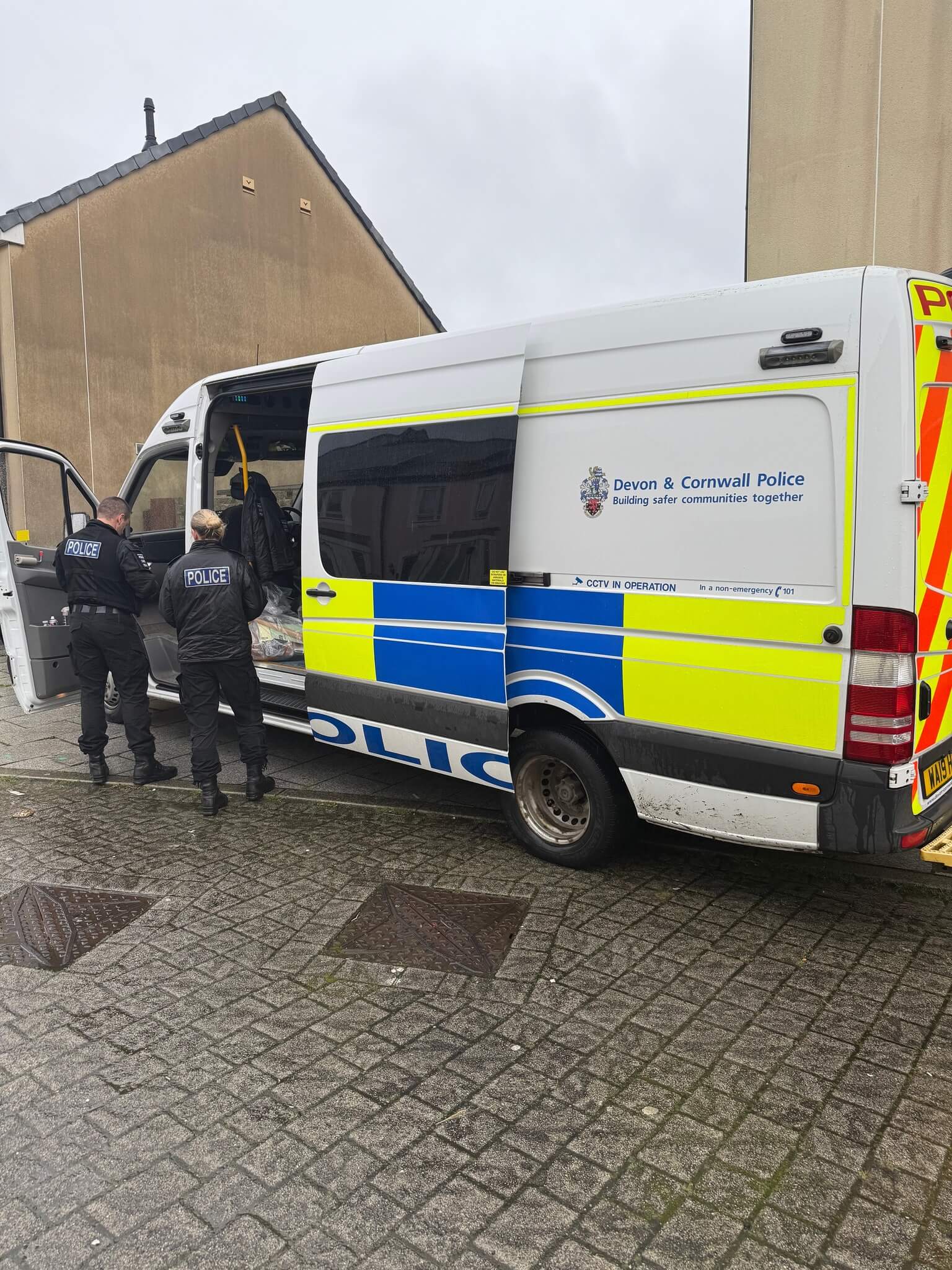 Devon and Cornwall Police officers at the open rear doors of a police van during a warrant operation in Tresillian