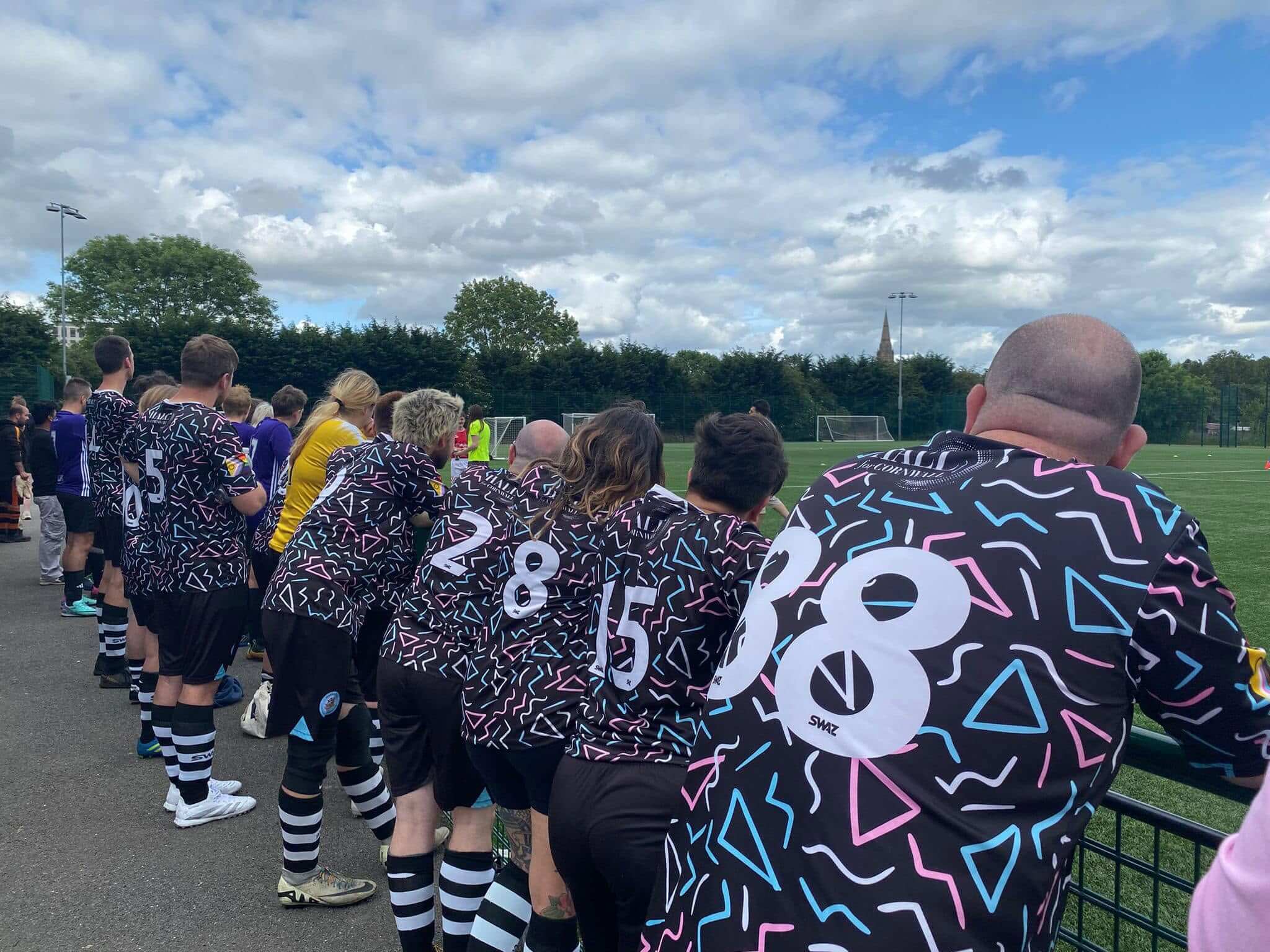 Stargazy FC players lined up pitchside in their black and pastel patterned kit
