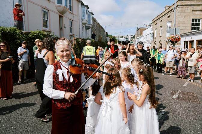 The fiddler smiles as she plays surrounded by the maids in a St Ives street