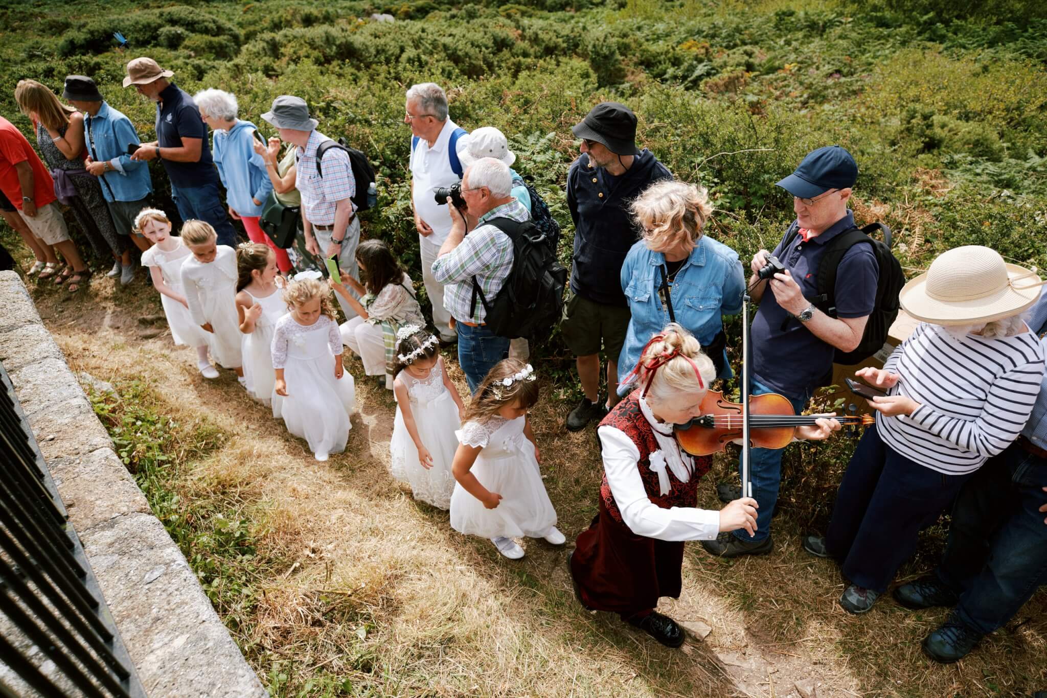 A fiddler in red velvet leads maids in white past a crowd on Worvas Hill above St Ives
