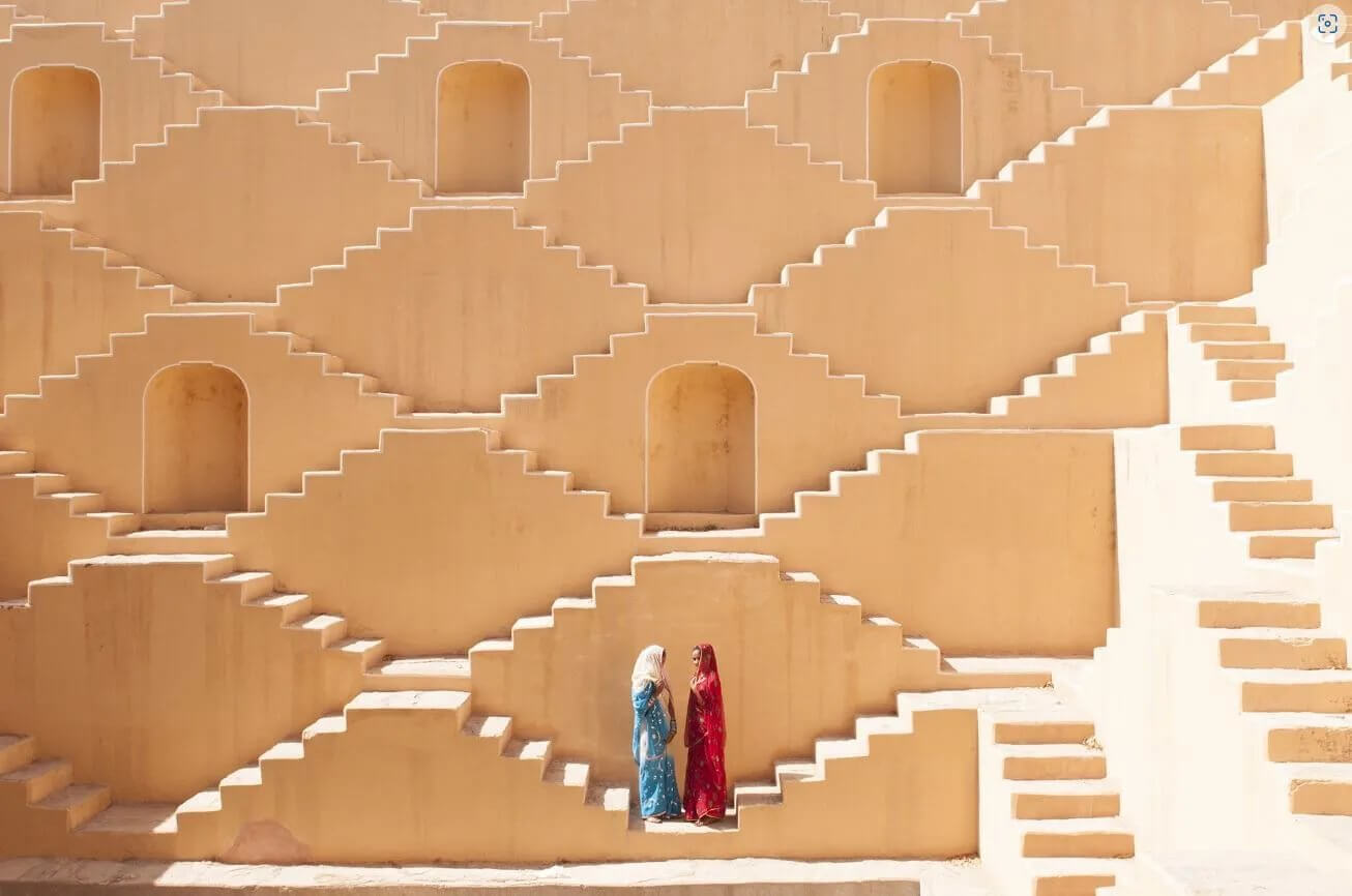 Two women in blue and red saris in the stepped walls of a stepwell in Jaipur, India, photographed by Ami Vitale