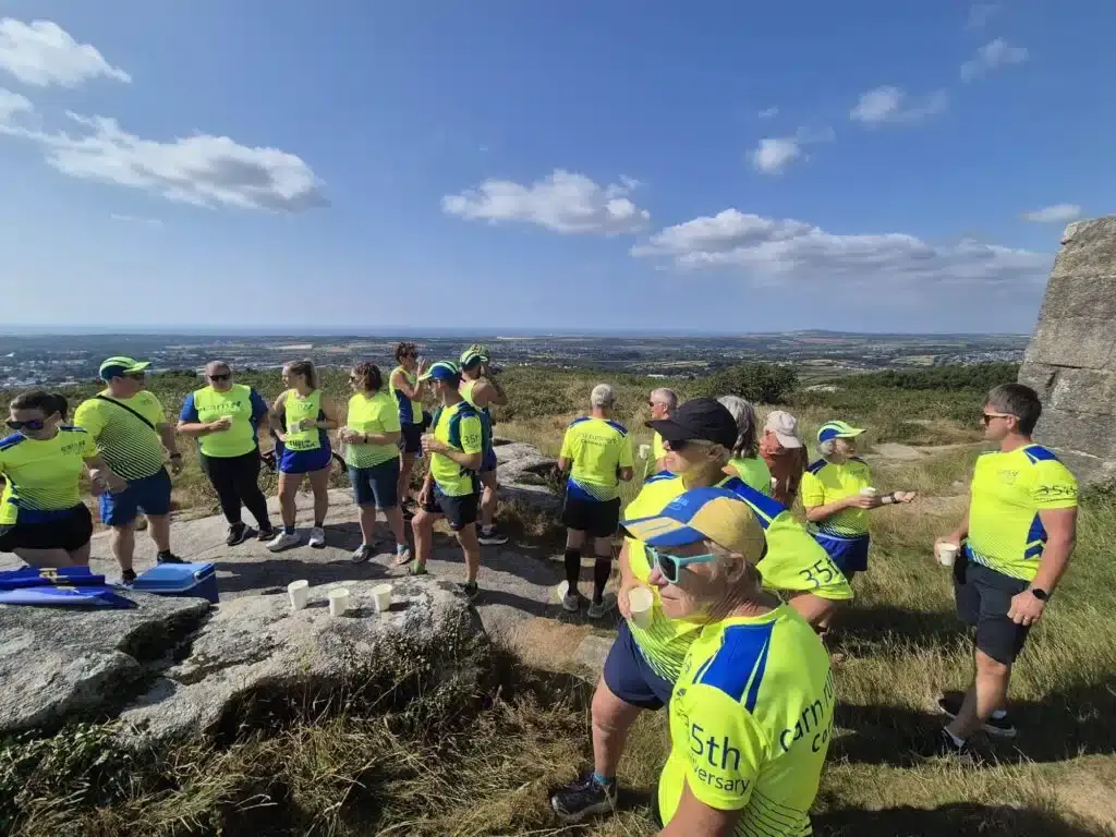 Carn Runners members toasting the club's 35th anniversary on top of Carn Brea, the countryside stretching out behind them