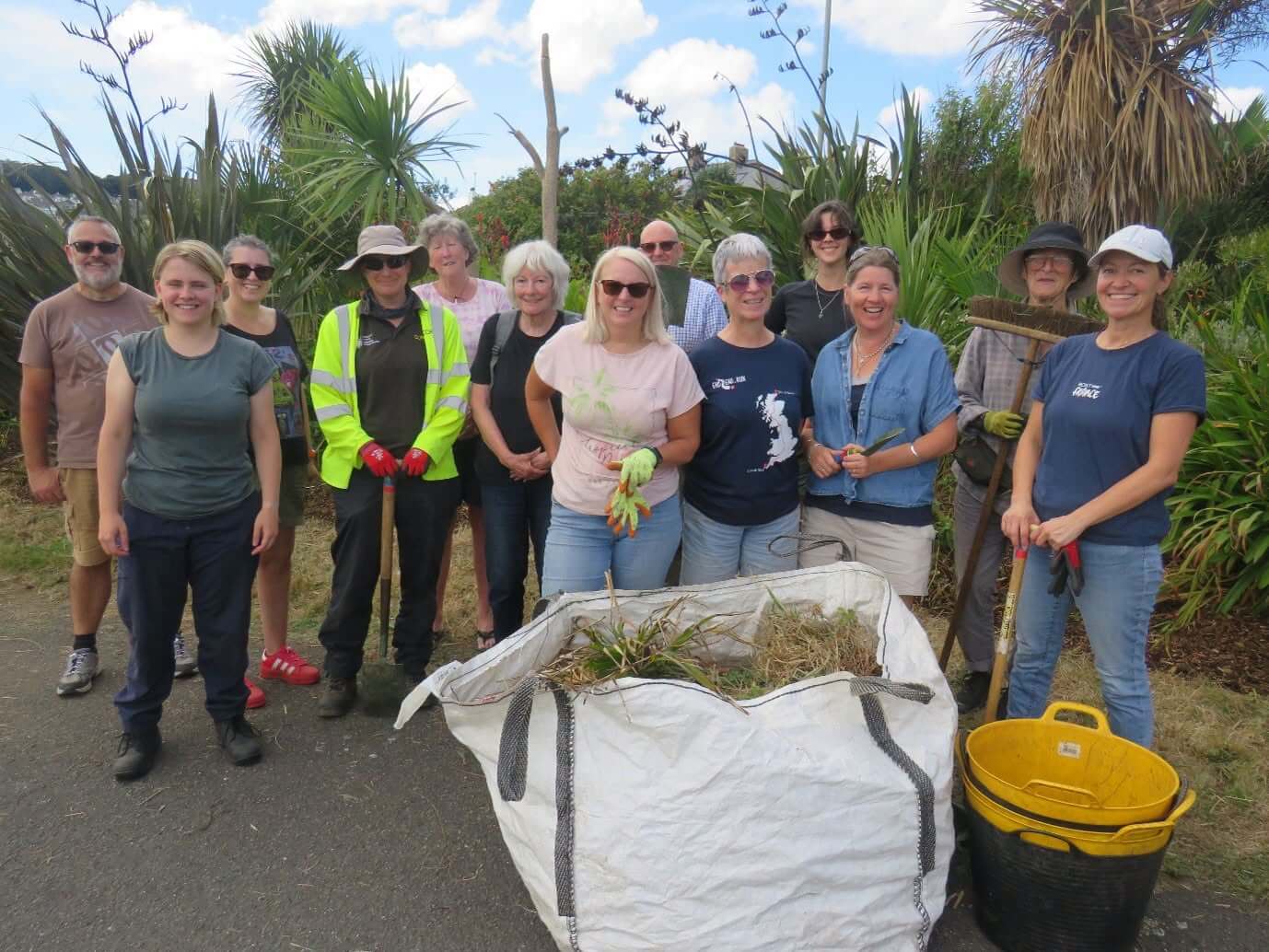 The group of Bolitho Gardens volunteers smiling behind a full bag of green waste