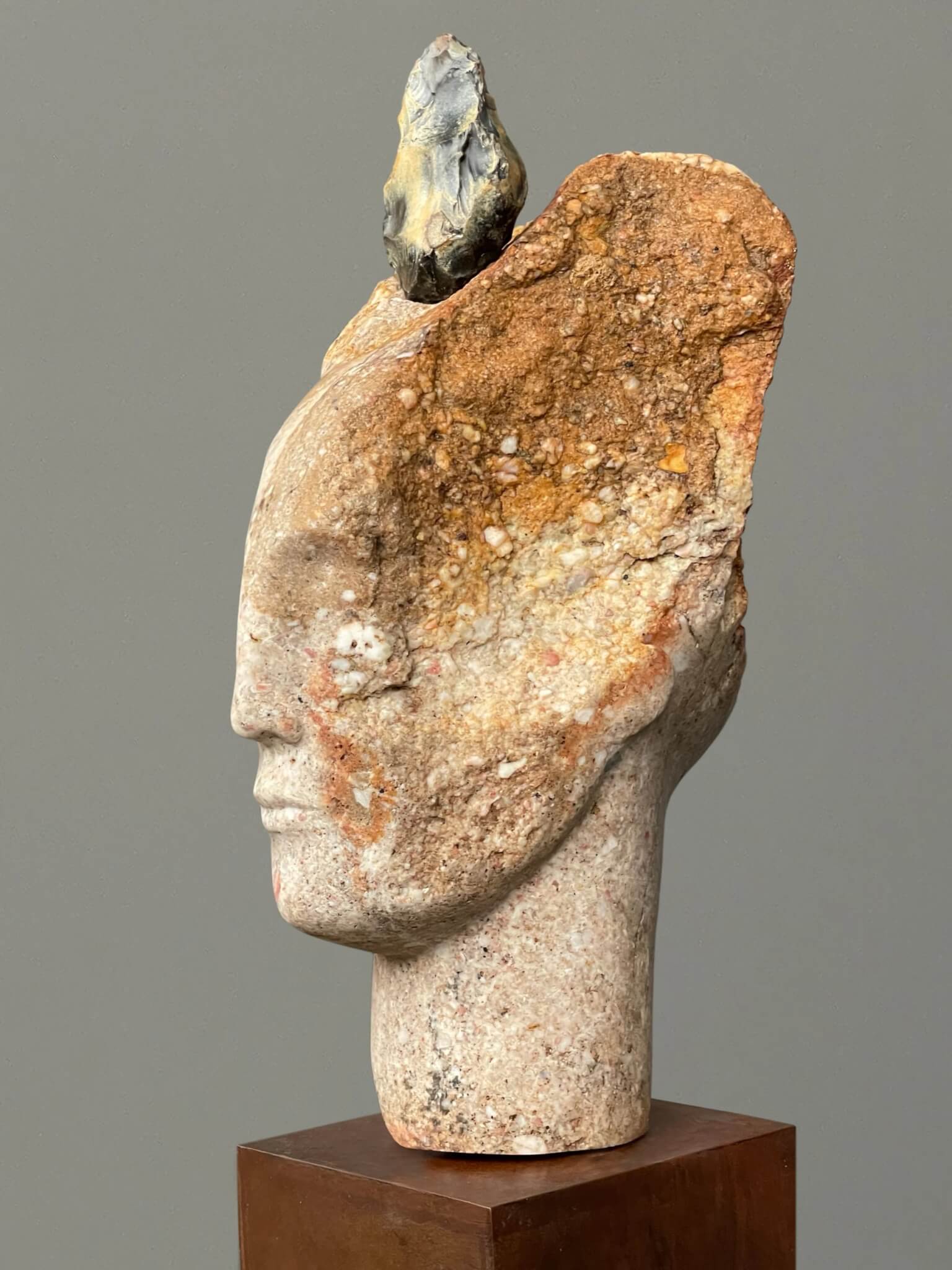 A carved stone face by Emily Young topped with an ancient flint hand axe, mounted on a metal plinth