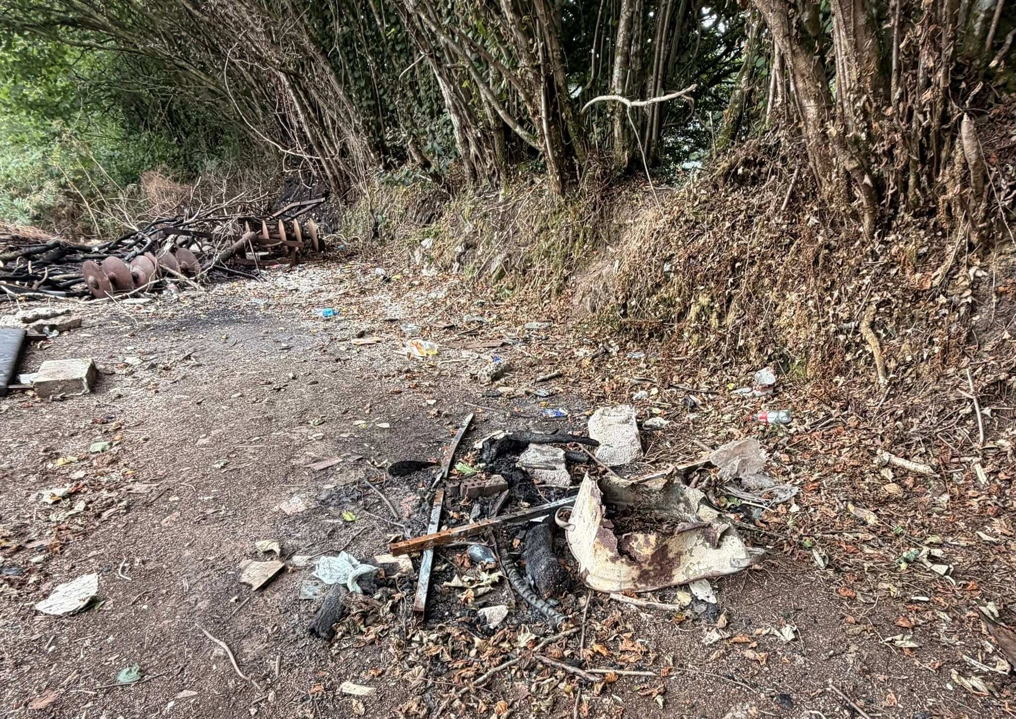 Old farm machinery and scattered litter on a track scorched by fire