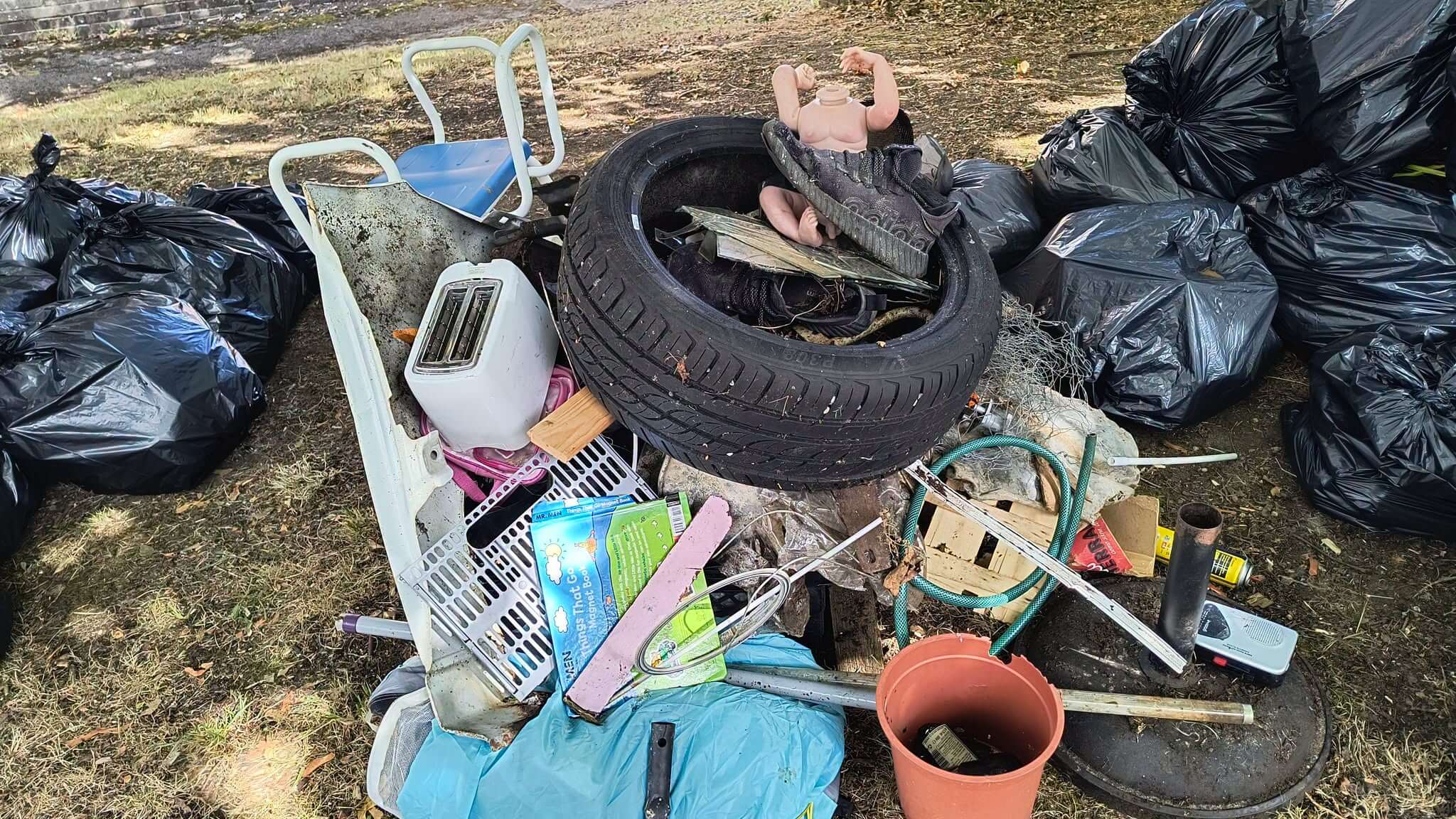 A pile of dumped items including a tyre, toaster, walking frame chair and a headless doll collected during the litter pick