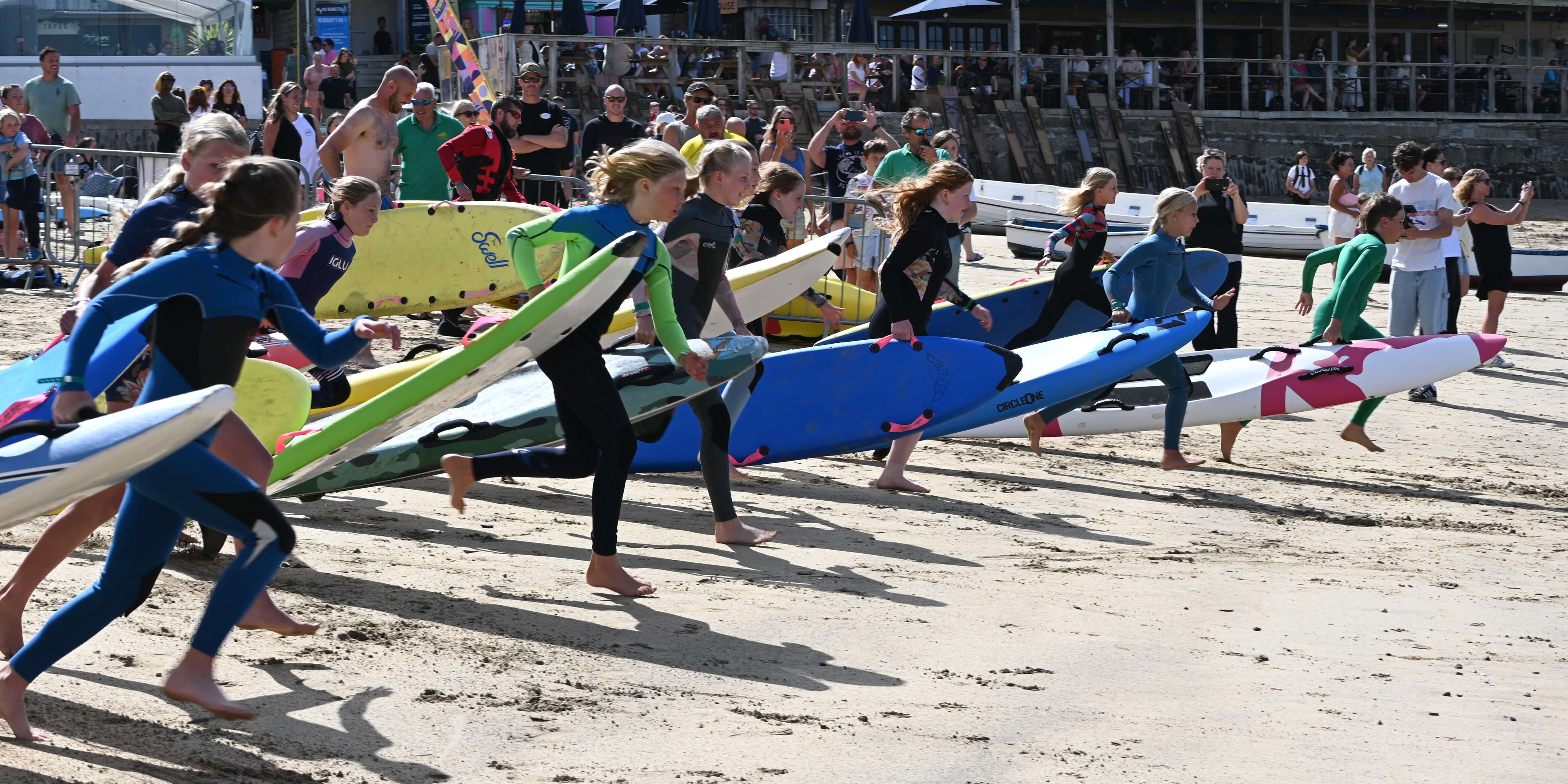 Young surf lifesavers sprint across Newquay beach carrying rescue boards as a crowd watches