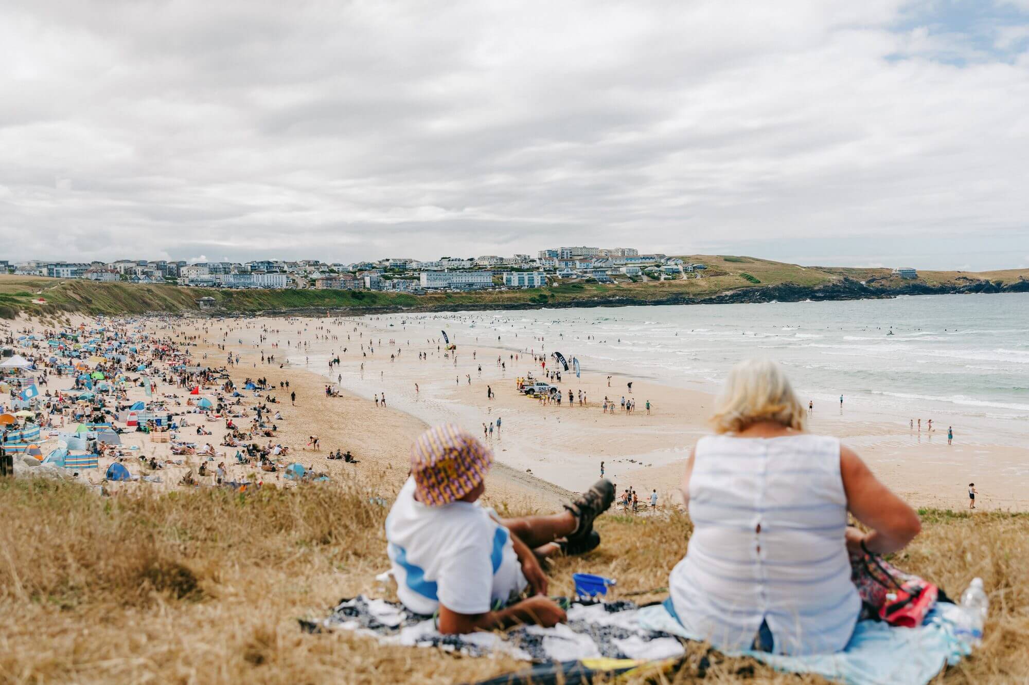 Two people watch the Boardmasters crowds and surf from the dunes above Fistral Beach