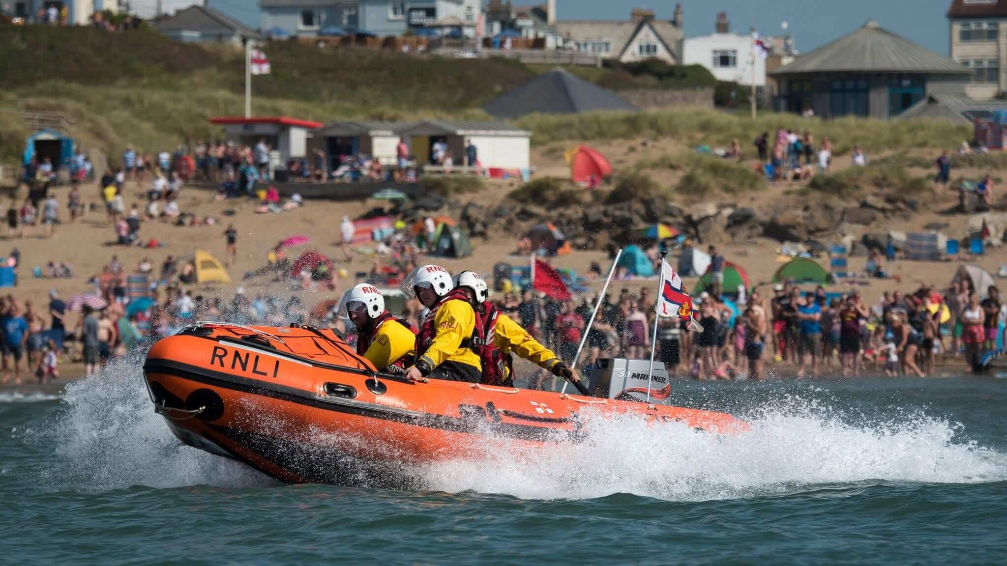 Bude RNLI inshore lifeboat crew powering past a packed beach during Lifeboat Weekend