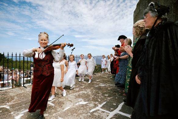The fiddler plays at the Knill Steeple as the widows in black applaud