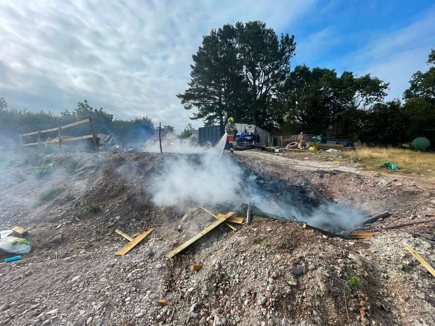 Firefighter damping down a smouldering bonfire on rough ground in Saltash