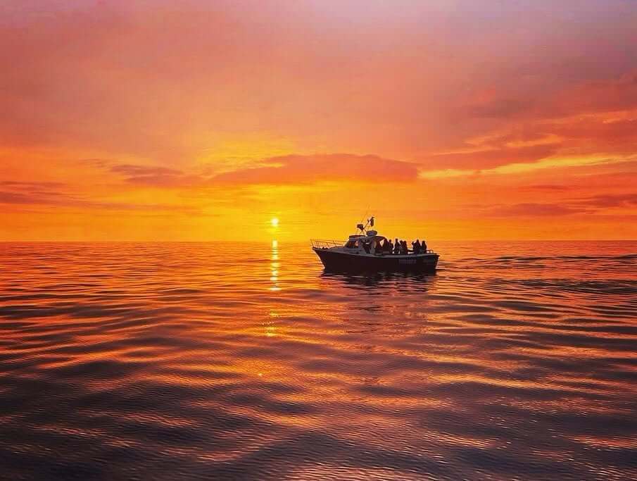 A boat trip out at sea during a bright orange sunset off St Ives