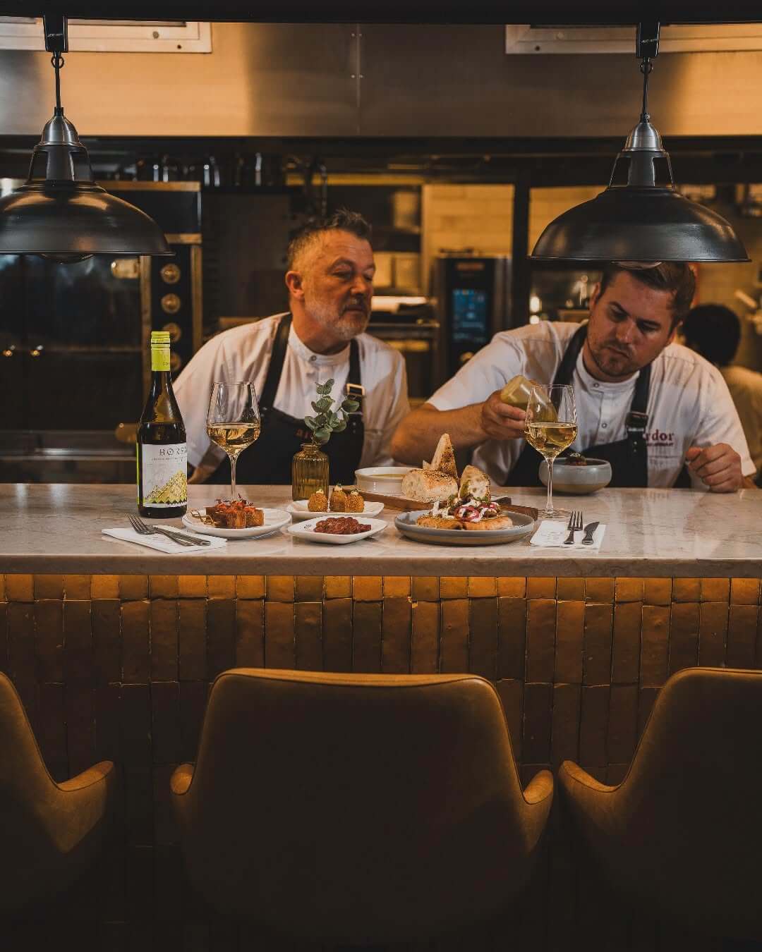Two chefs plating small dishes at a restaurant chef's counter