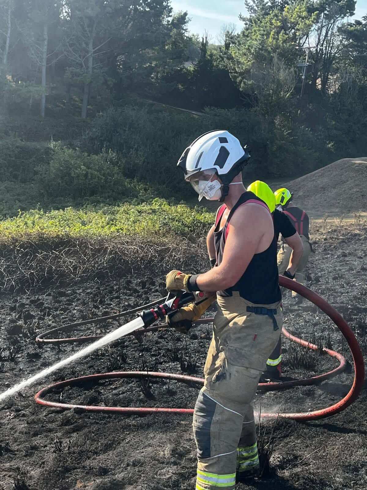 Firefighter damping down a scorched field with a hose