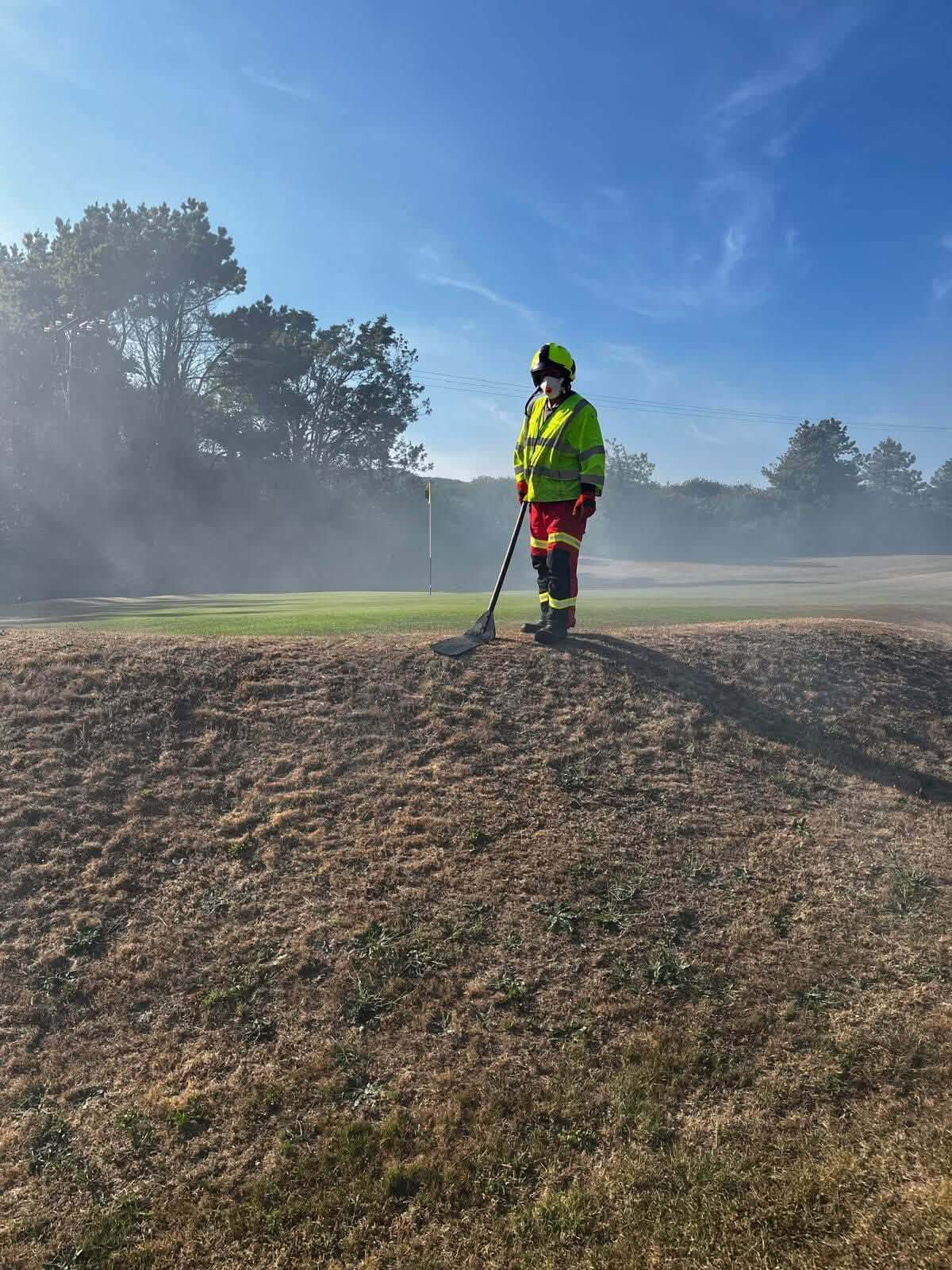 Firefighter with a beater standing watch beside a golf green in the smoke