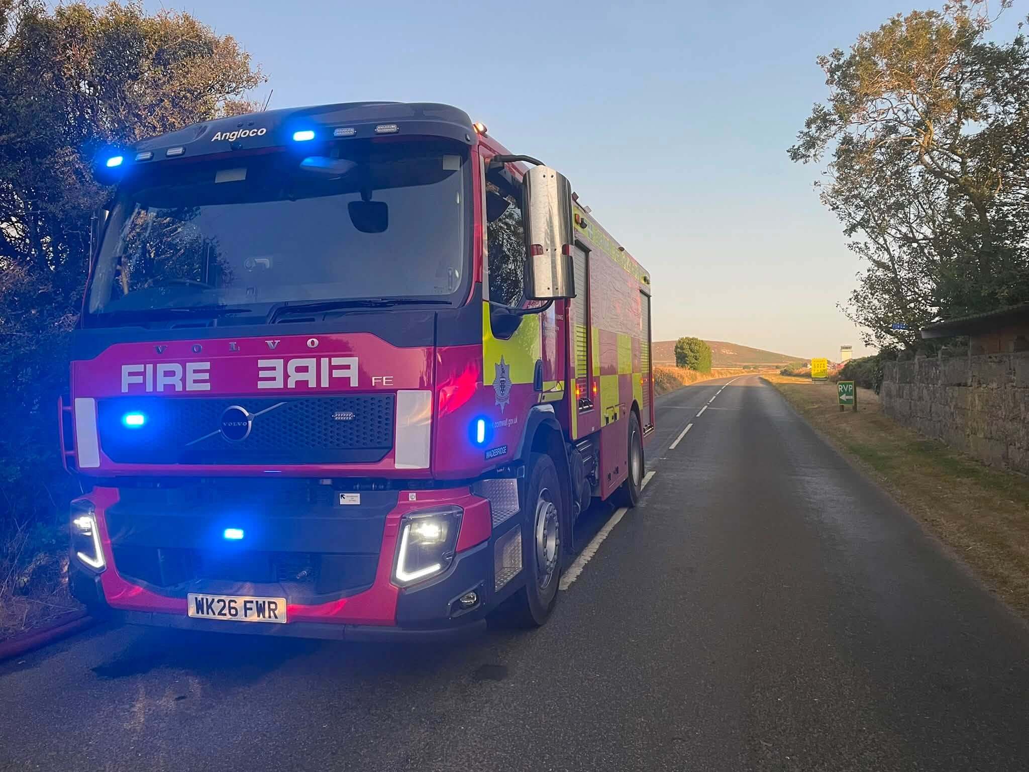 A Cornwall Fire and Rescue Service engine parked on a rural road near Wadebridge at dusk with its blue lights on