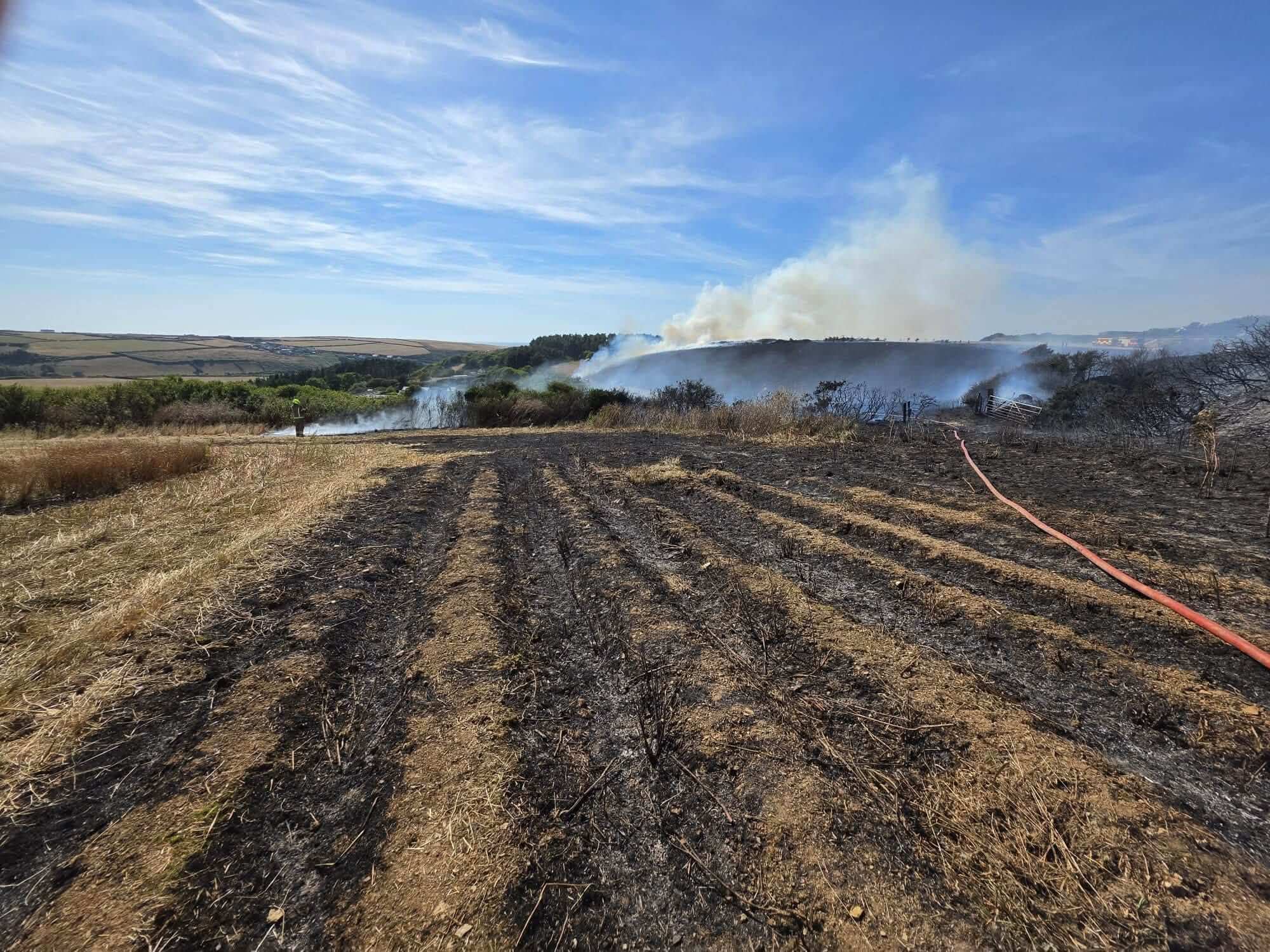 Wide view of a scrubland fire with a large smoke plume over a Cornwall hillside