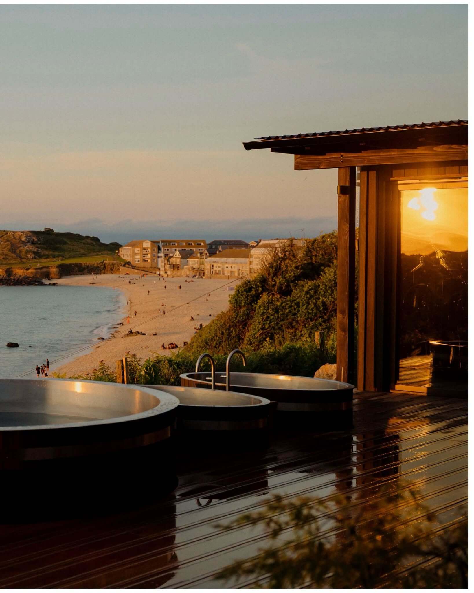 A sauna deck with hot tubs overlooking a St Ives beach at sunset