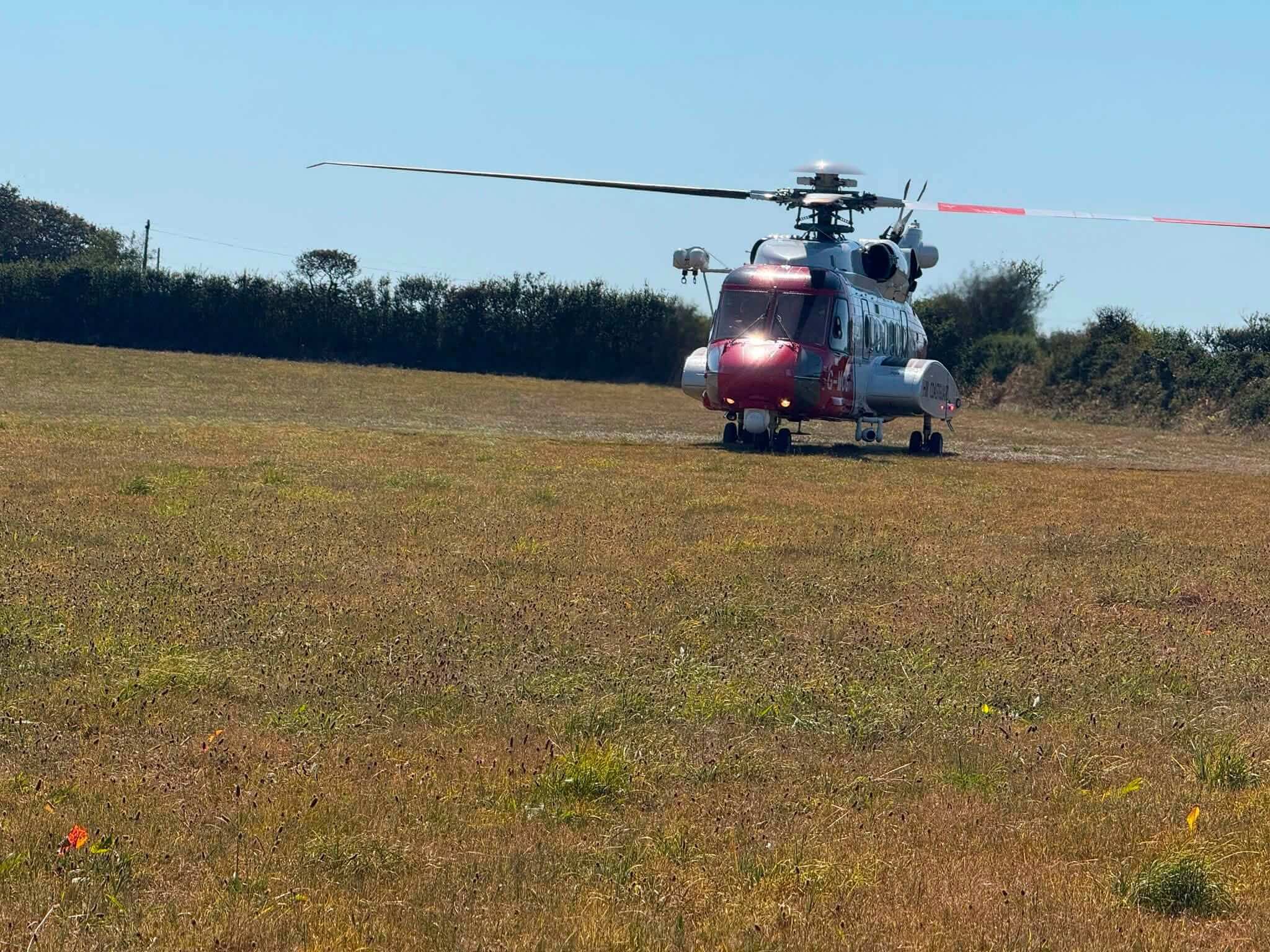 Coastguard search and rescue helicopter on the ground in a field near the coast
