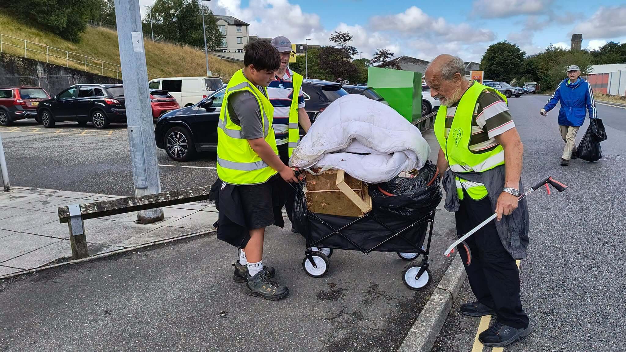 Volunteers wheeling a cart loaded with fly-tipped items including a mattress topper