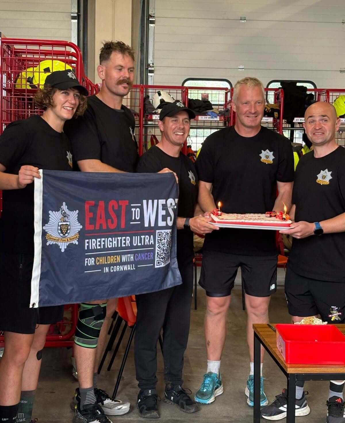 St Austell Community Fire Station's Green Watch celebrating with a cake and East to West Firefighter Ultra flag