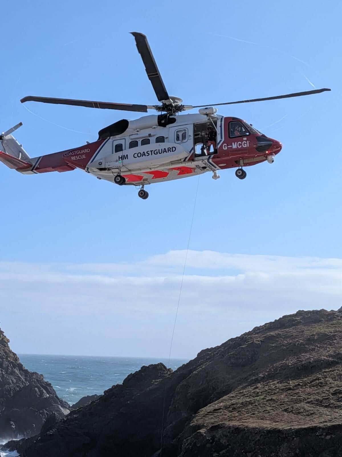 HM Coastguard helicopter G-MCGI flying low over cliffs near Kynance Cove