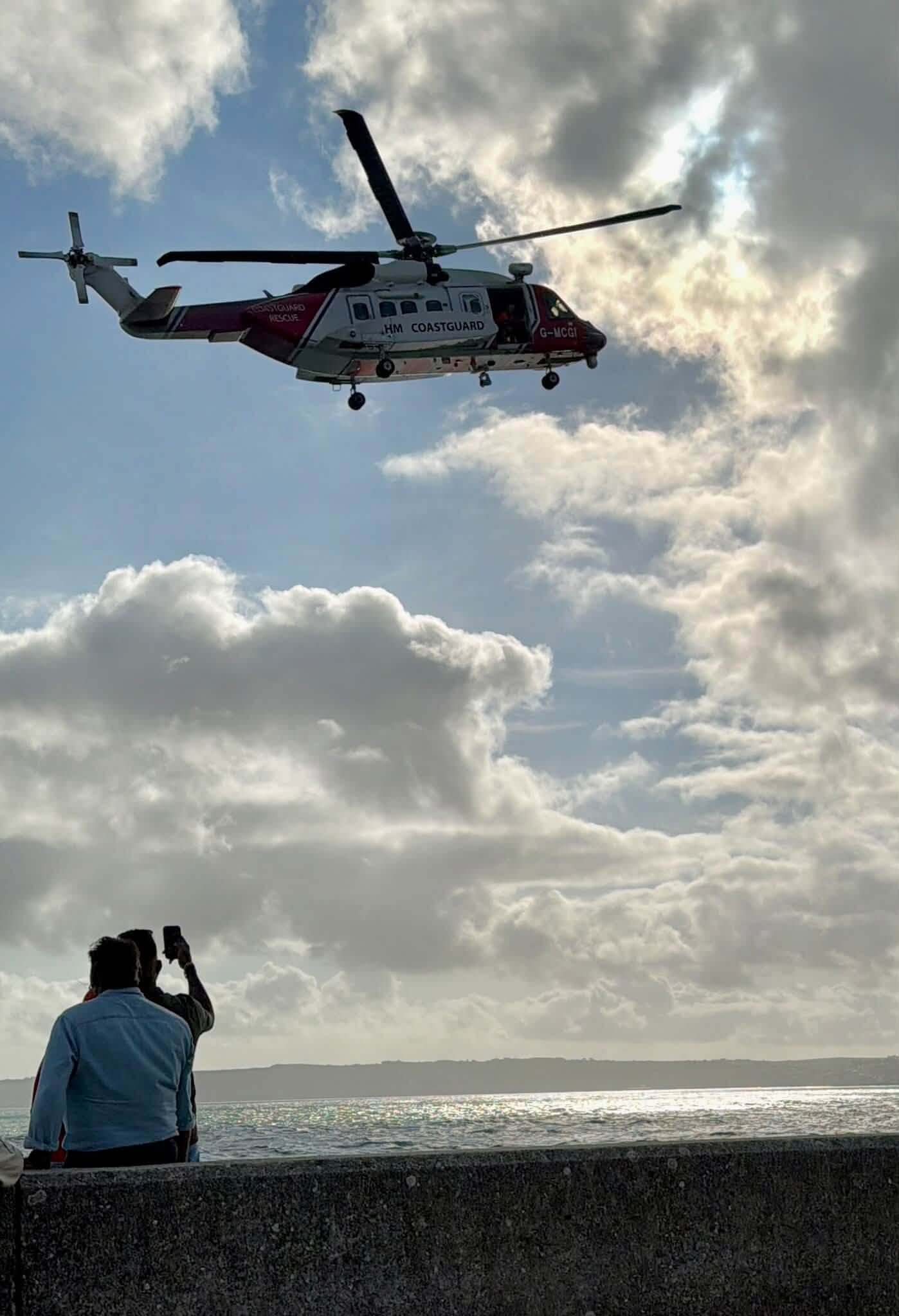 Members of the public watch and film the HM Coastguard helicopter over Marazion seafront