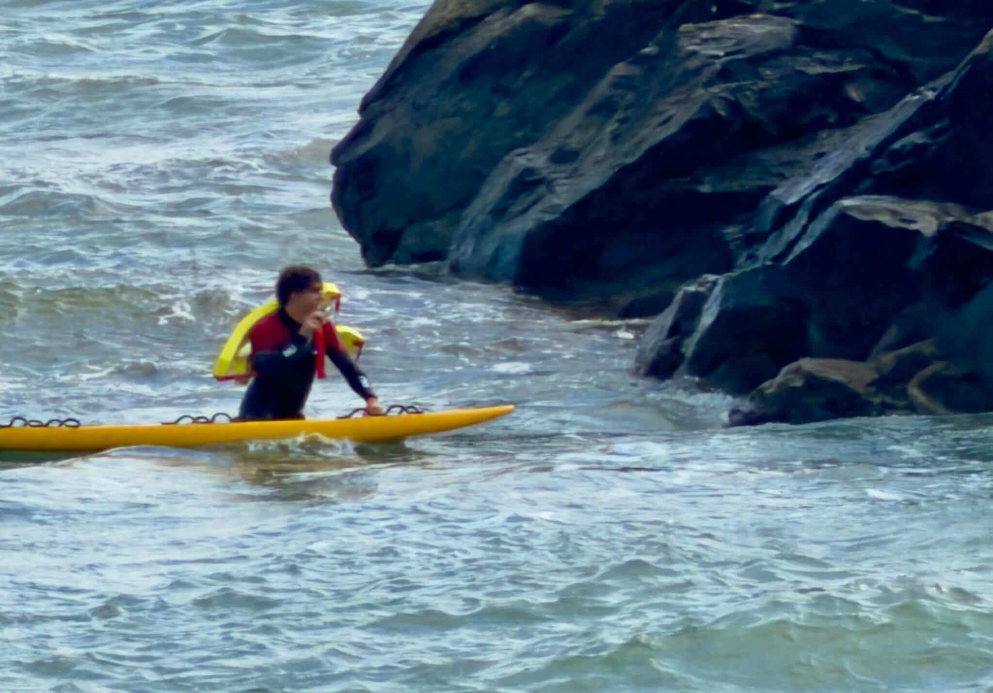 An RNLI lifeguard on a rescue board in the water near the rocks off Marazion