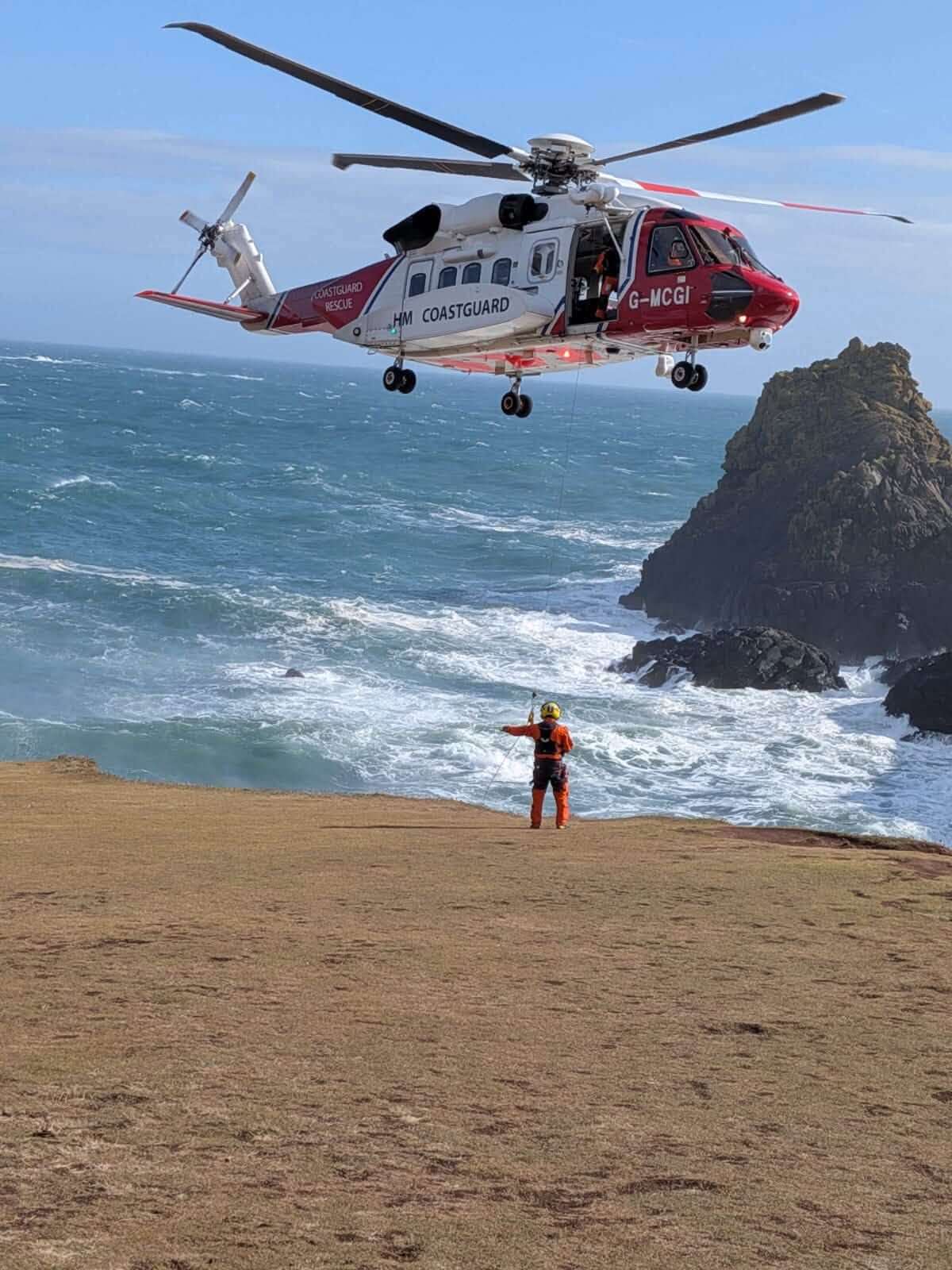 HM Coastguard rescue helicopter SAR 924 hovering over cliffs with a coastguard officer on the clifftop