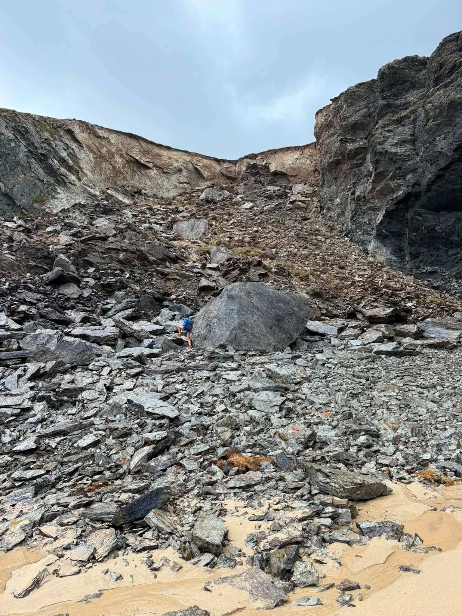 A person beside the scale of the rockfall at Holywell Bay