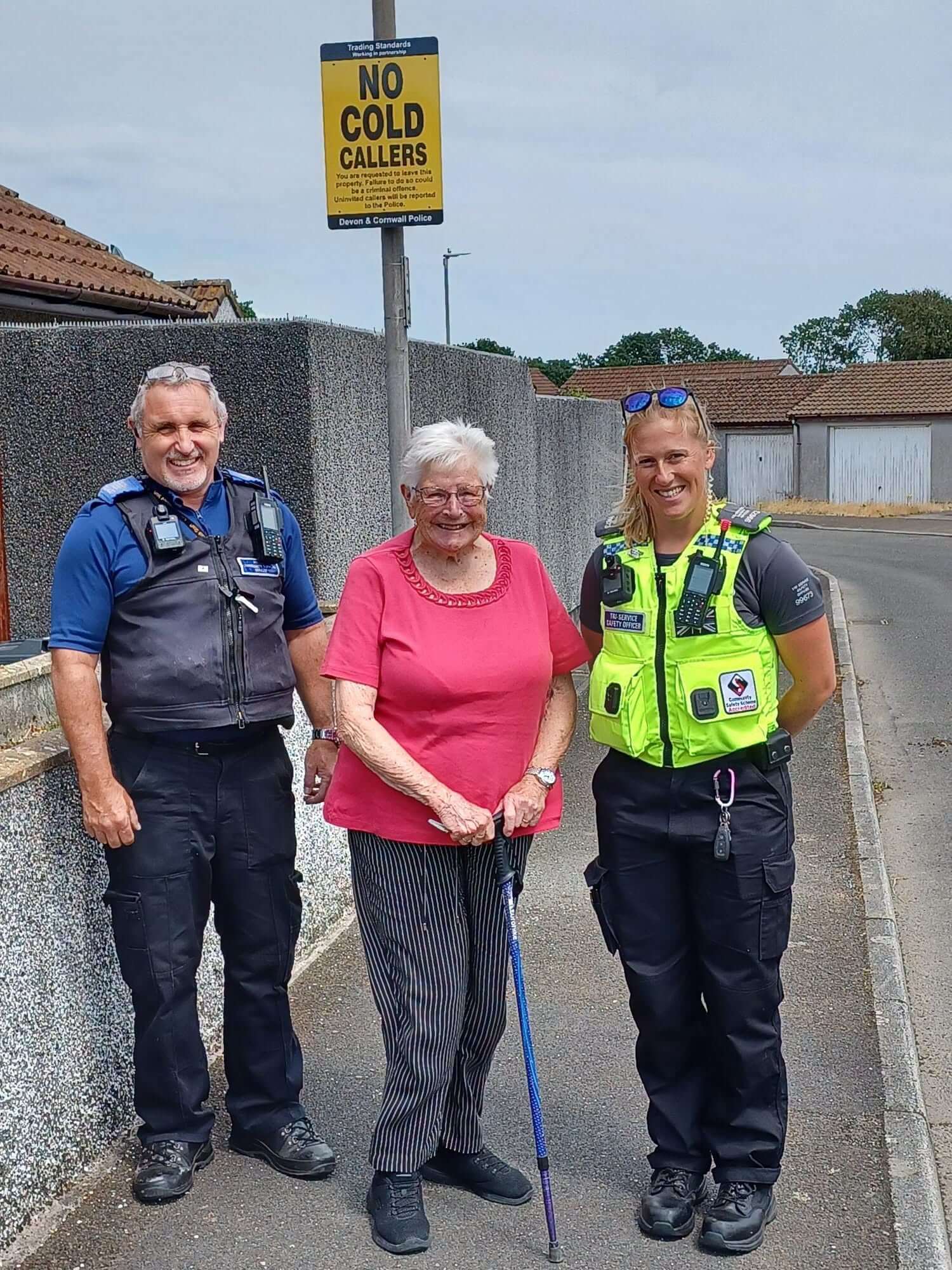 An older resident stands with two officers next to a No Cold Callers sign