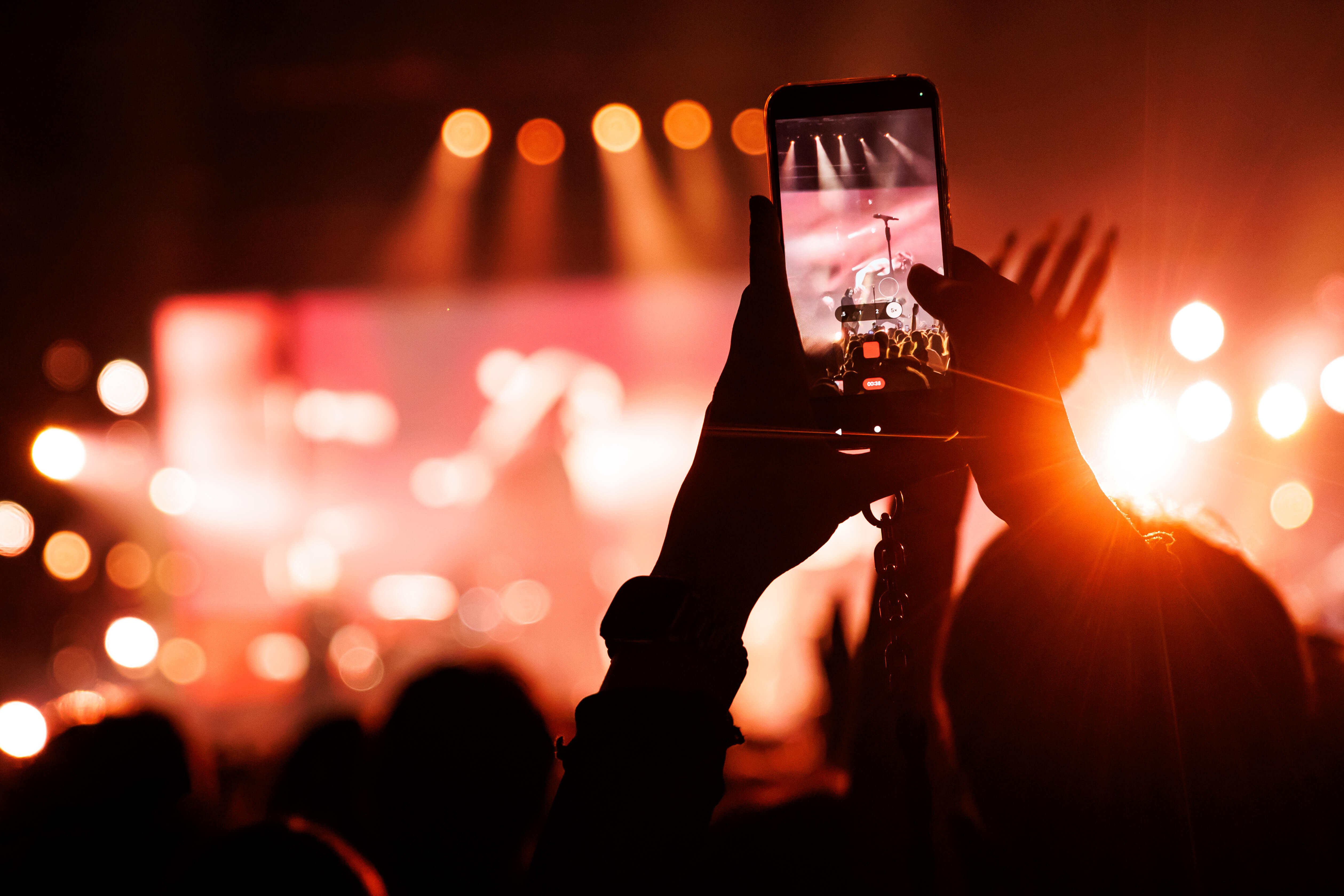 A festivalgoer holding up a phone to film a band on a floodlit stage