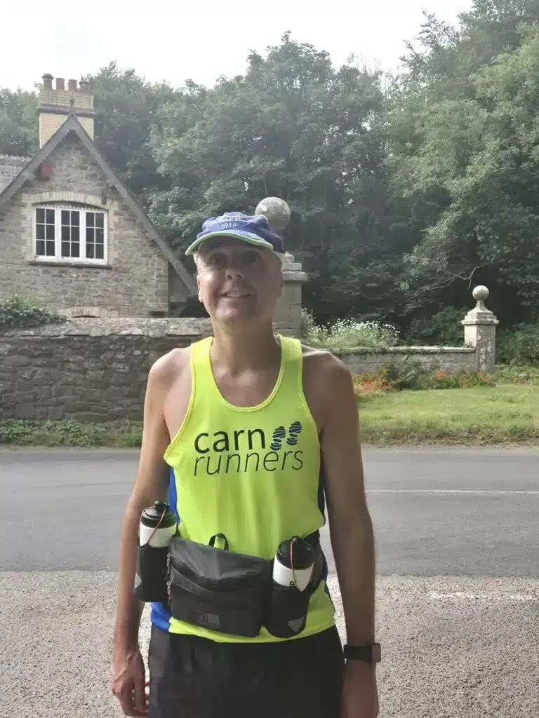 A Carn Runner in a yellow club vest and running belt on a country road