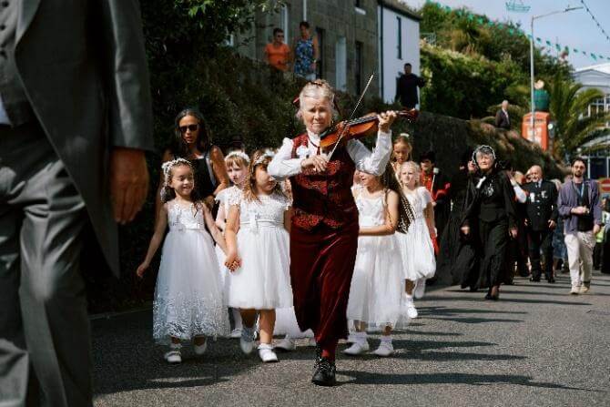 The fiddler leads the maids and two widows in black through the streets of St Ives
