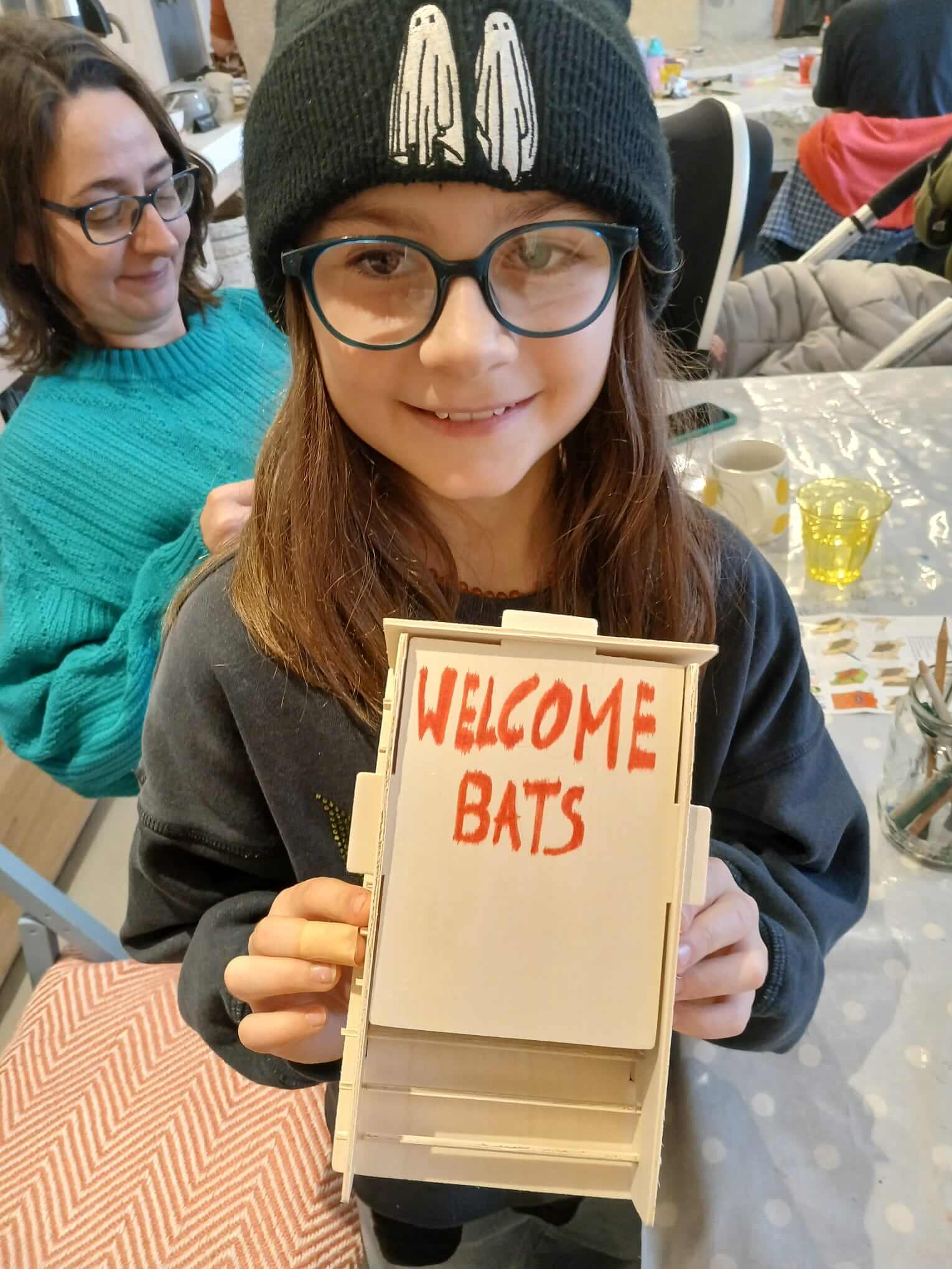 A child holds a wooden bat box painted with the words Welcome Bats