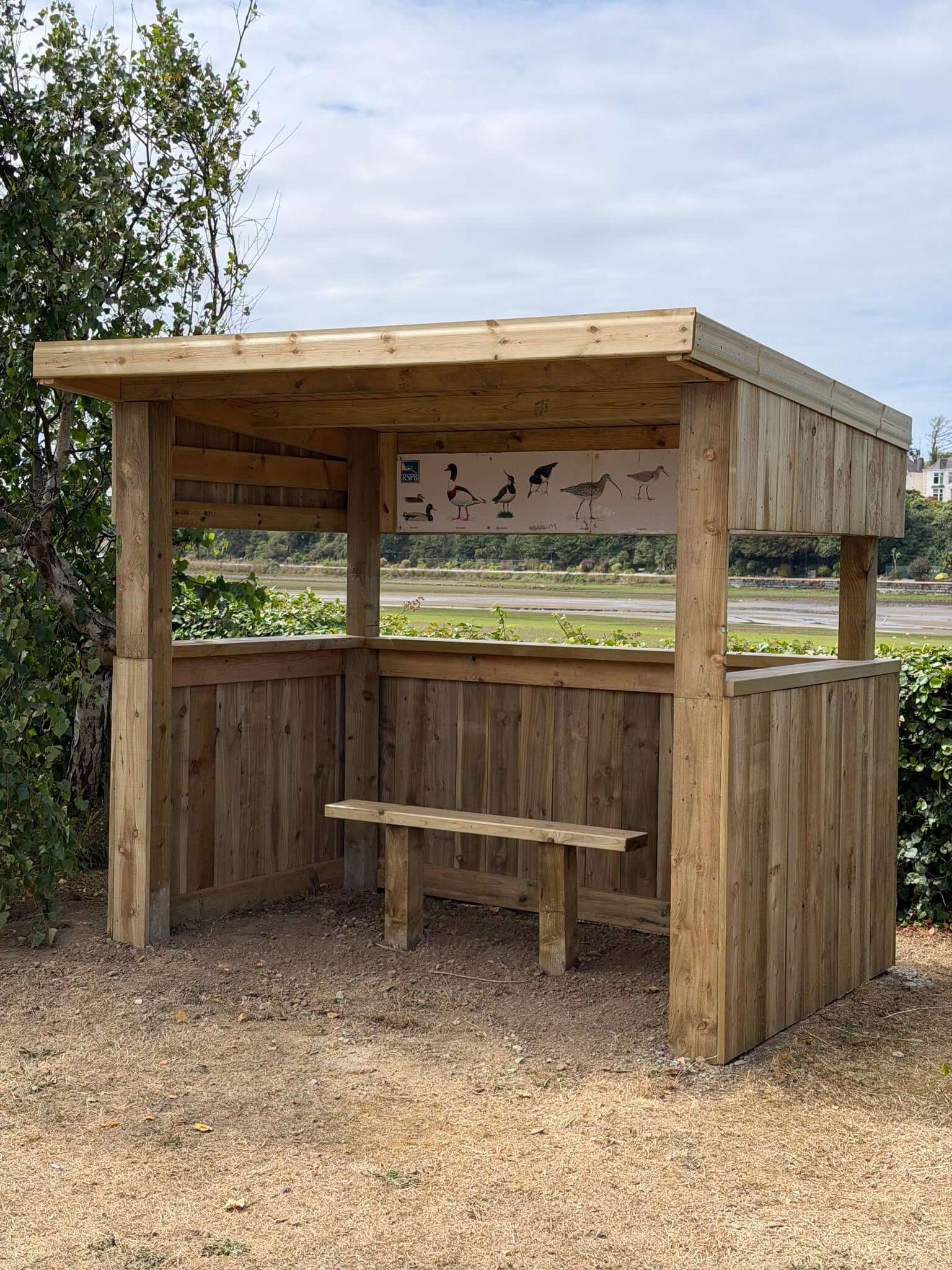 The new Hayle Library bird hide with a bench, RSPB identification board and open view across the estuary mudflats