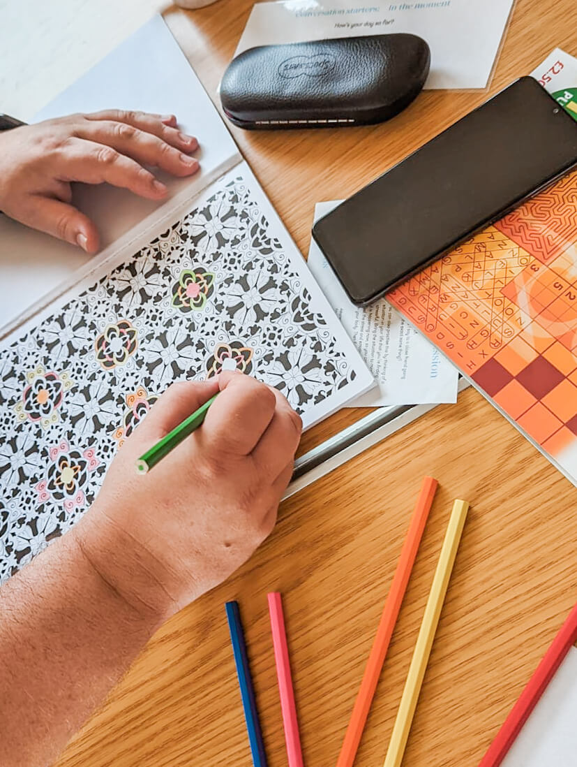 A hand colouring in a patterned page with coloured pencils on a wooden table