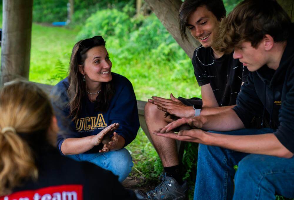 A facilitator and three young people laughing during a hands-on nature session in the greenery at the Eden Project