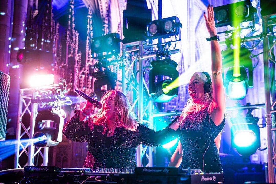The duo Dvotion performing, one singing into a microphone and one on the decks in headphones, under stage lighting
