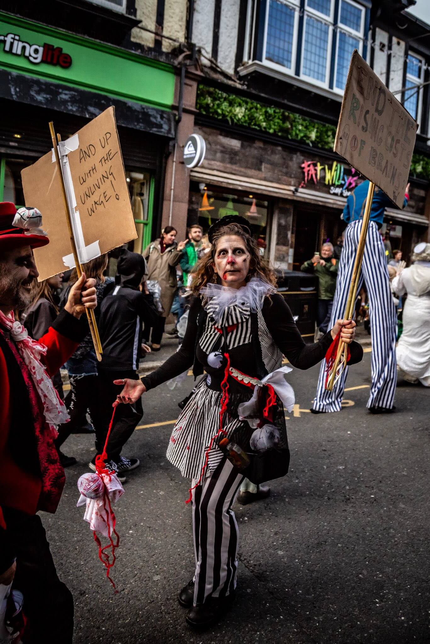 A zombie performer carries a placard during the Newquay Zombie Crawl