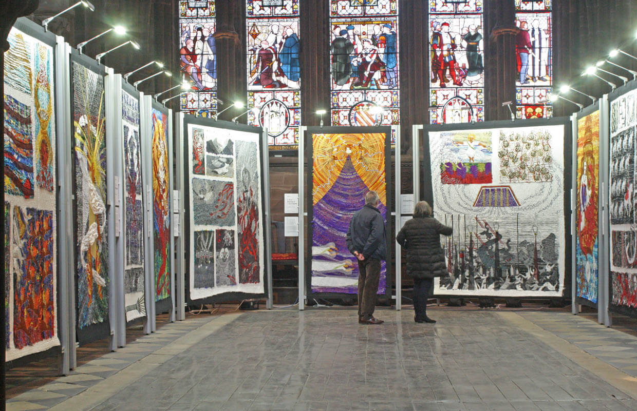Visitors looking at illuminated embroidered panels below stained glass