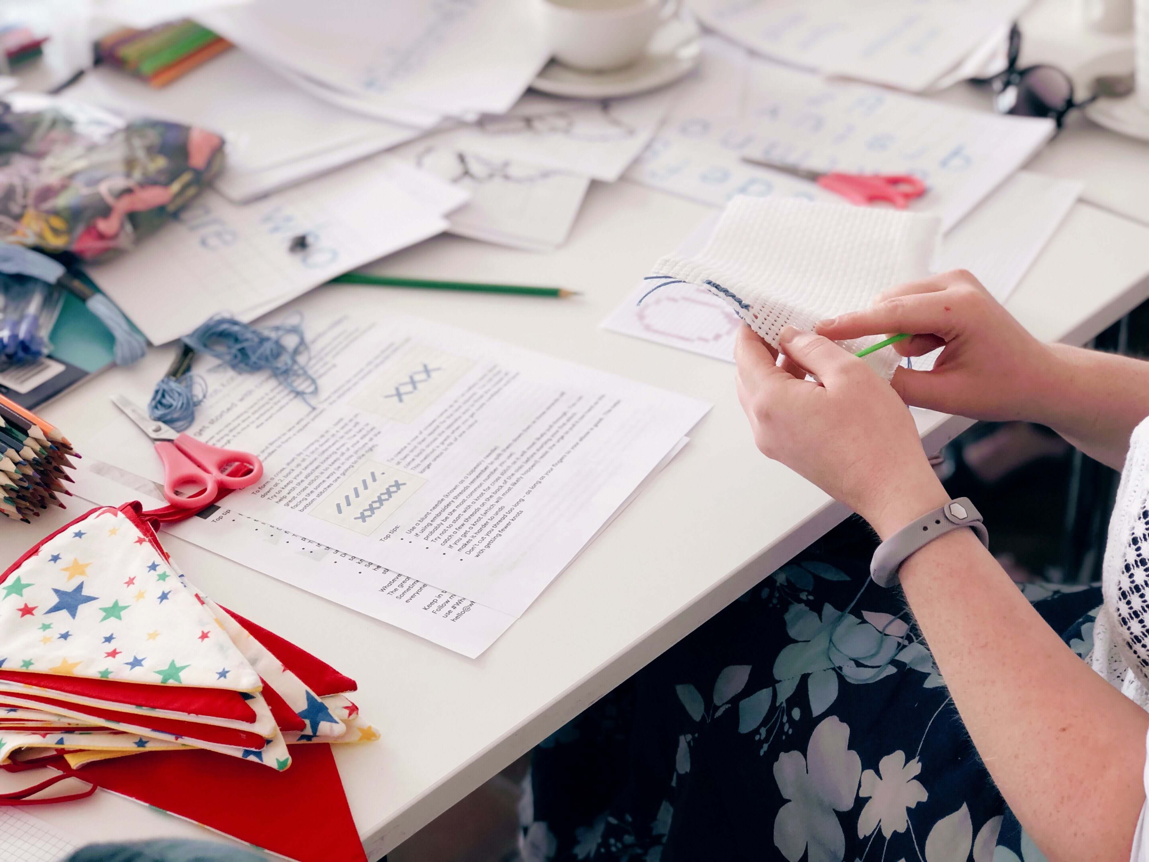 A table covered with wool, pompoms and craft materials with people working around it