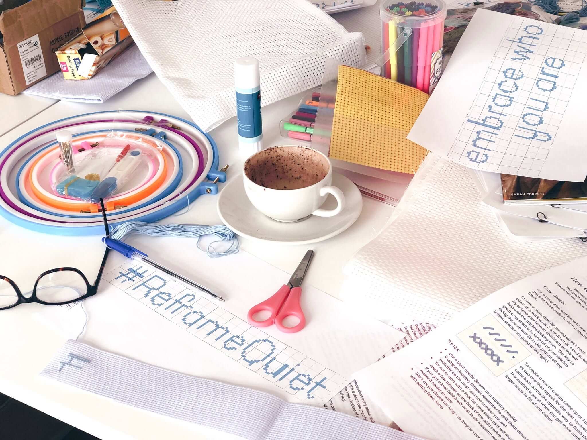 Cross stitch charts reading Reframe Quiet and embrace who you are, with hoops, thread and a cup of coffee