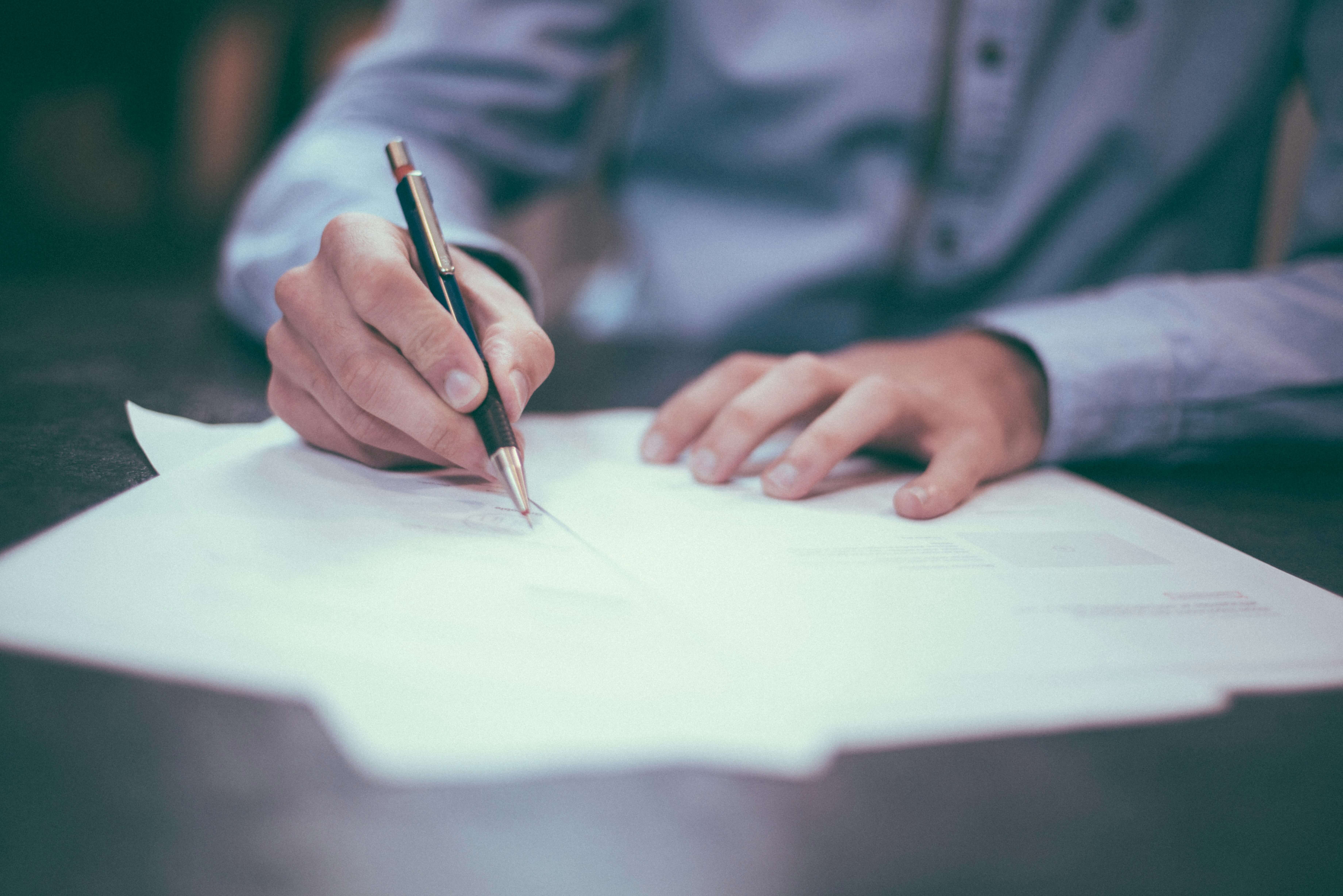 A person writing on a document with a pen at a desk