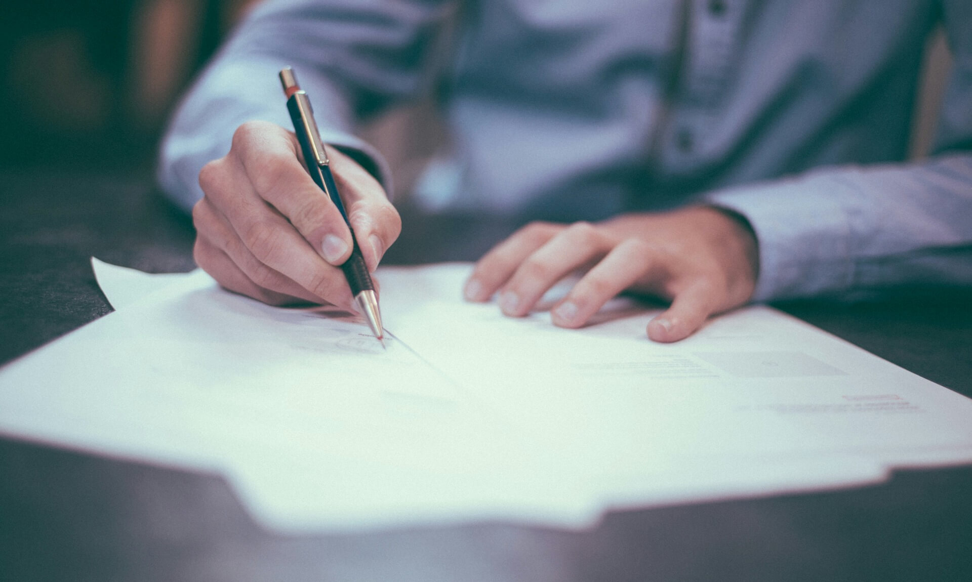 A person writing on a document with a pen at a desk