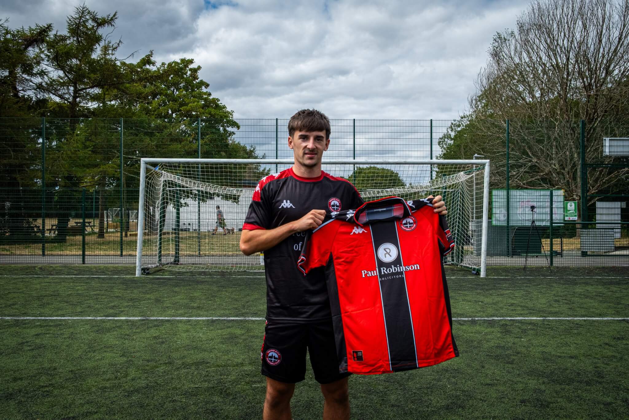 Tom Dean holding up the Truro City home shirt in front of a goal
