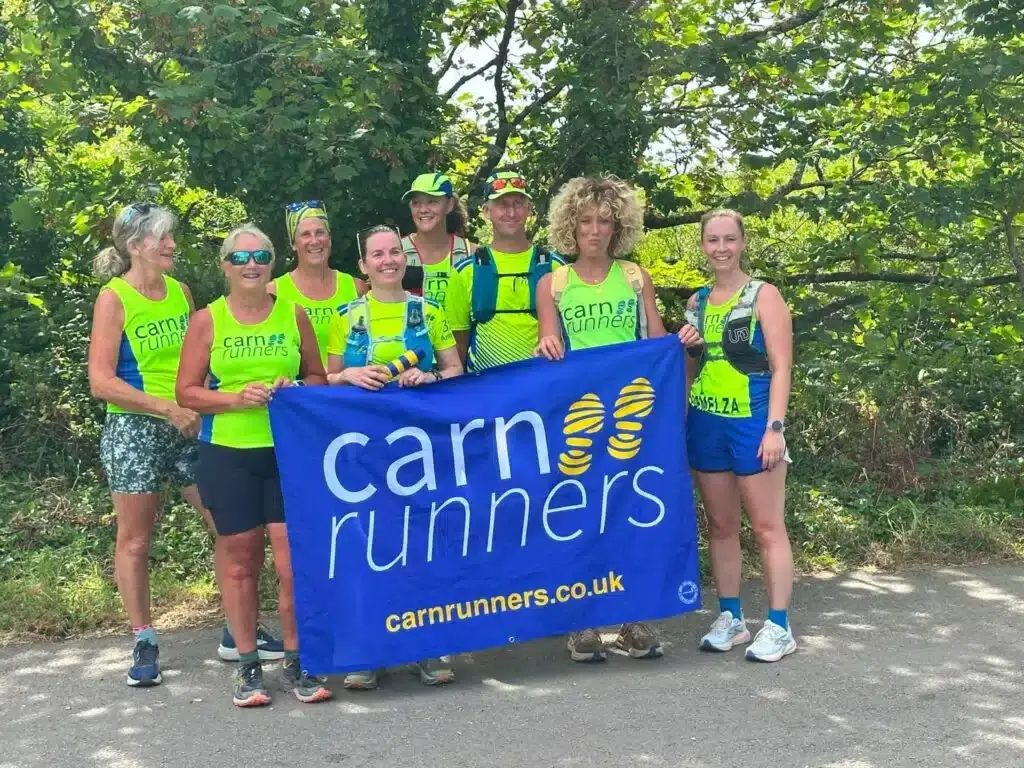 Eight Carn Runners in yellow vests holding the club's blue Carn Runners flag on a lane